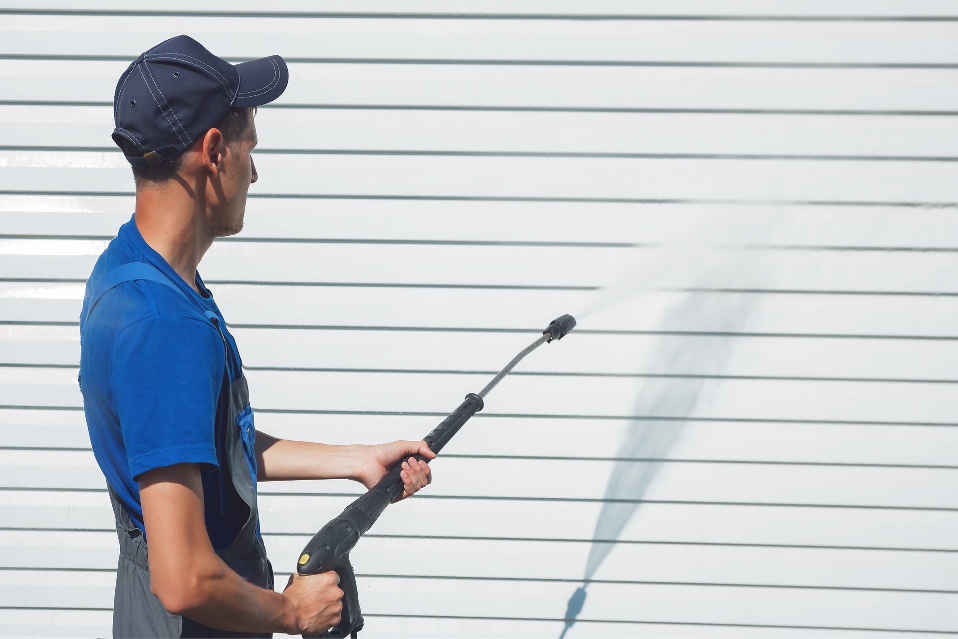 Man power washing a white, horizontal-paneled building.