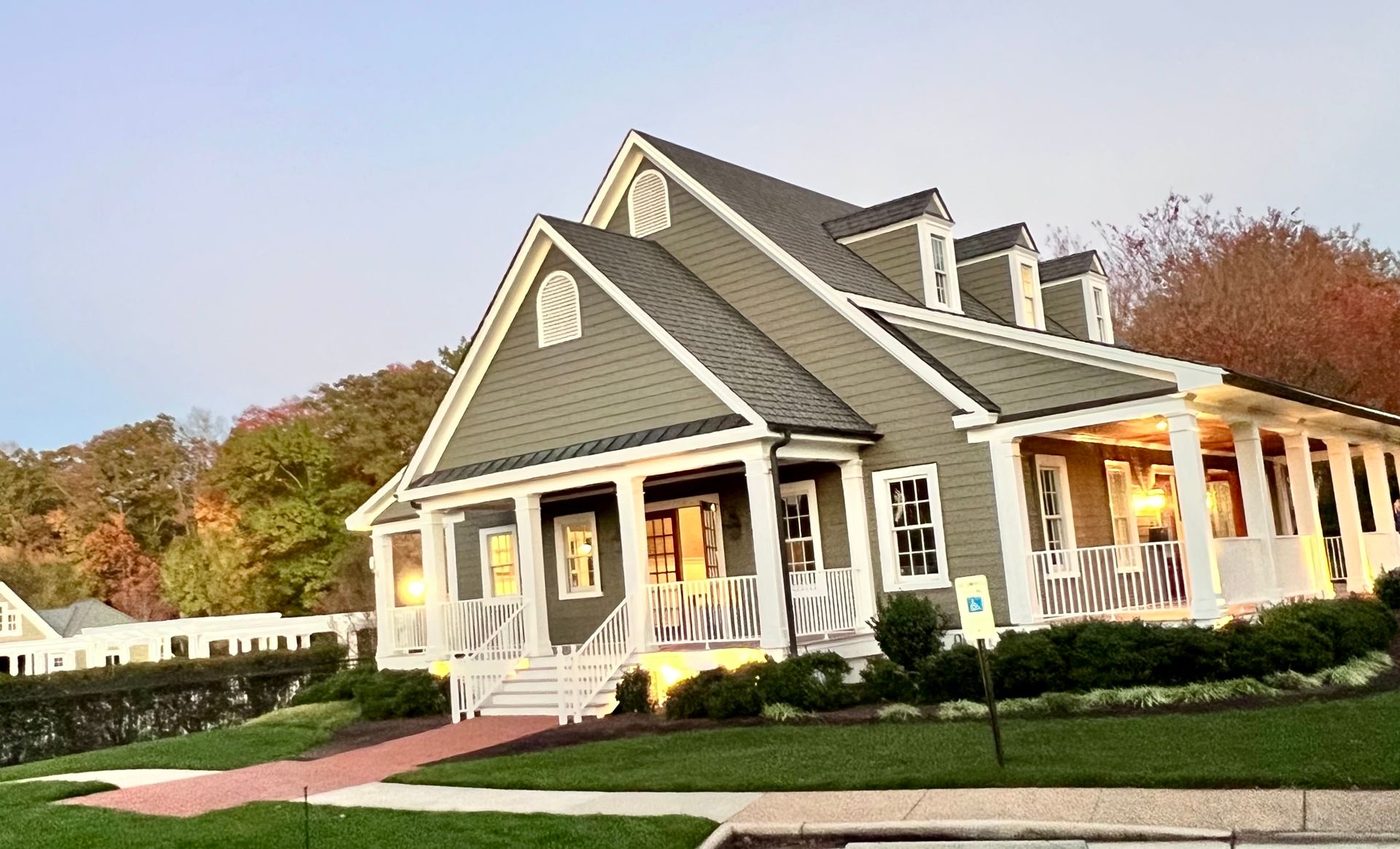 Green cottage-style building with white trim, porch, and dormers. Red brick pathway and green lawn.