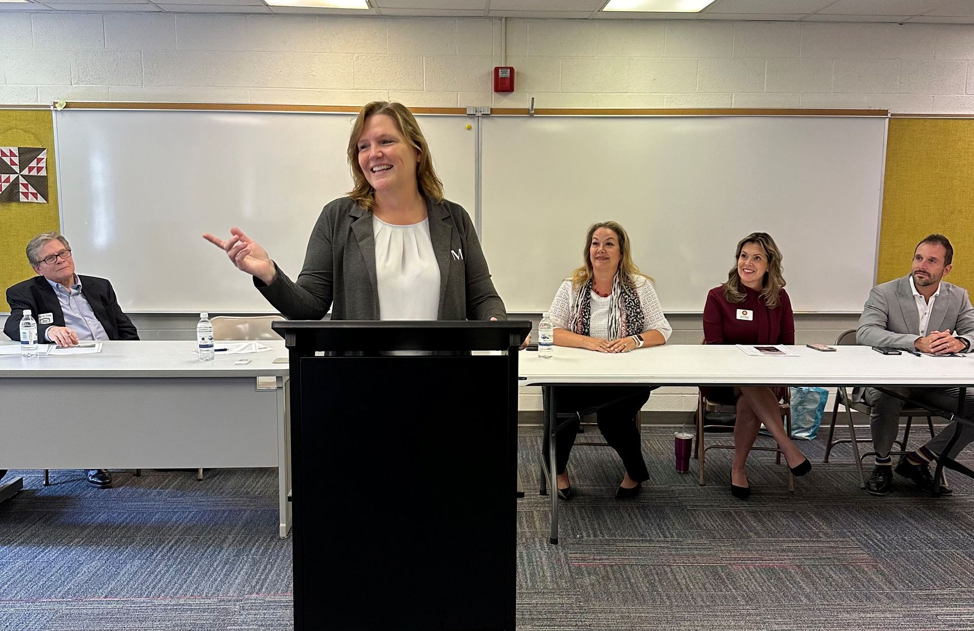 Leslie Hocker, co-founder of MINA is standing at a podium giving a speech in front of the MINA Legacy Panel.