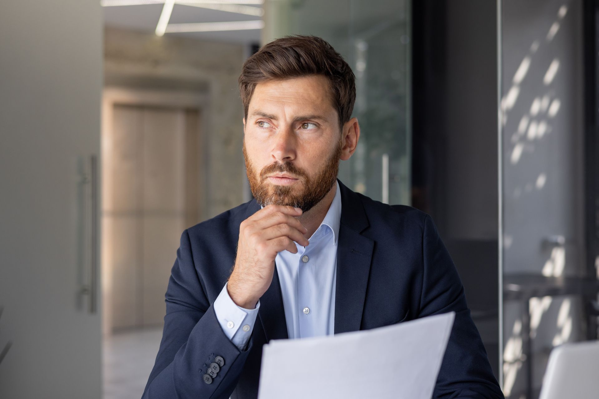 A man in a suit is sitting at a table with a document in his hand.