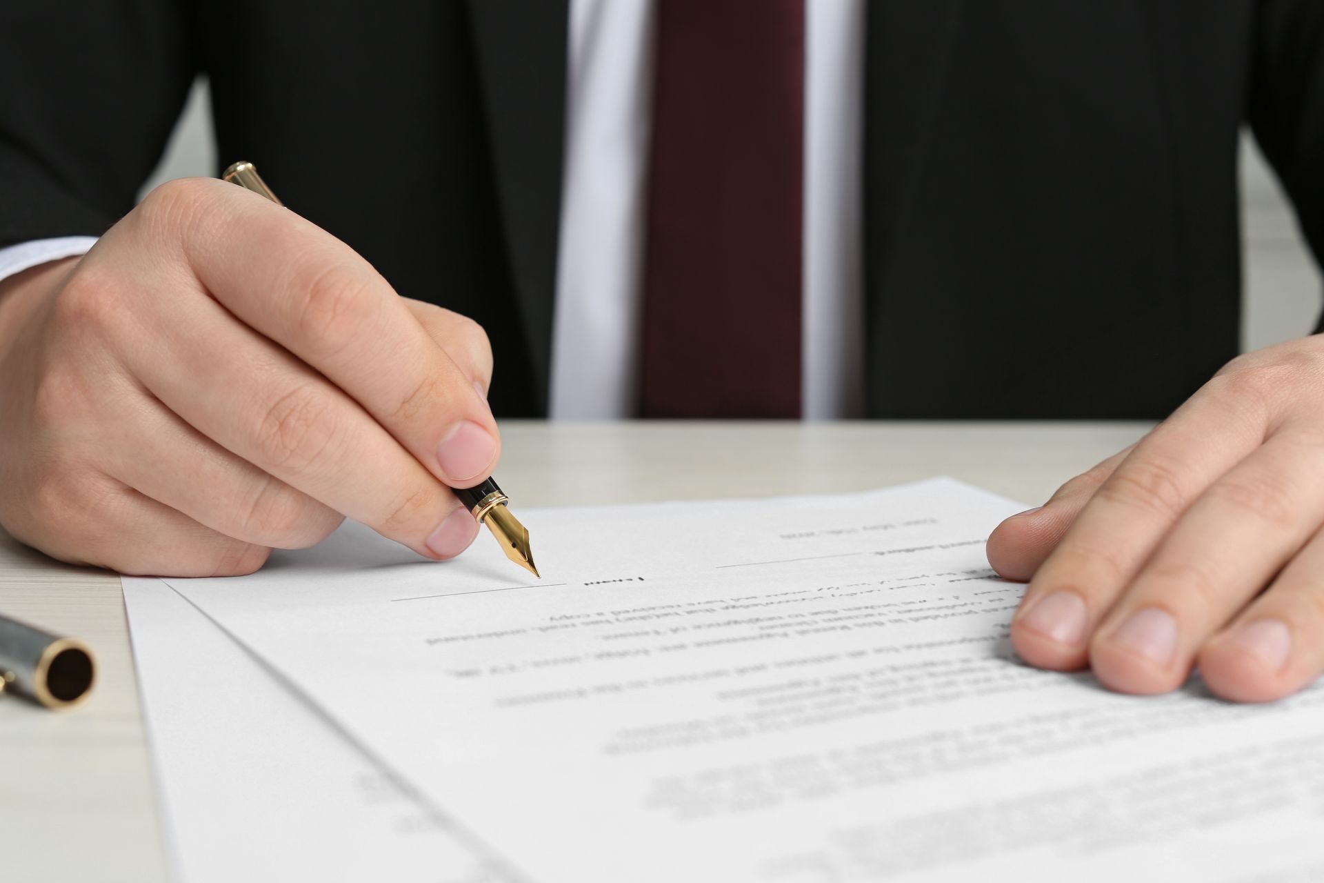 A notary public in a suit and tie is signing a piece of paper with a pen.