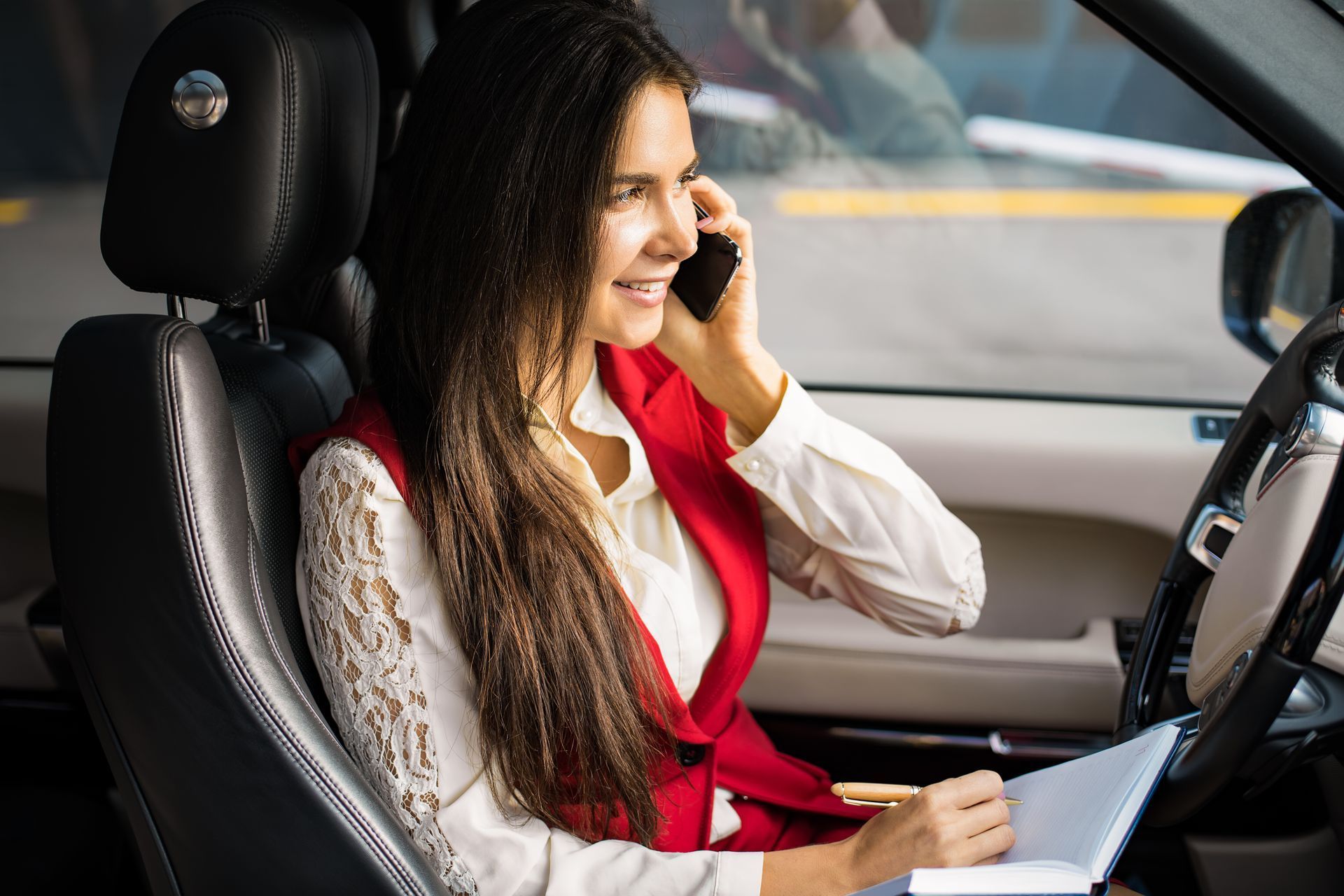 A woman is sitting in the driver's seat of a car talking on a cell phone making an appointment.