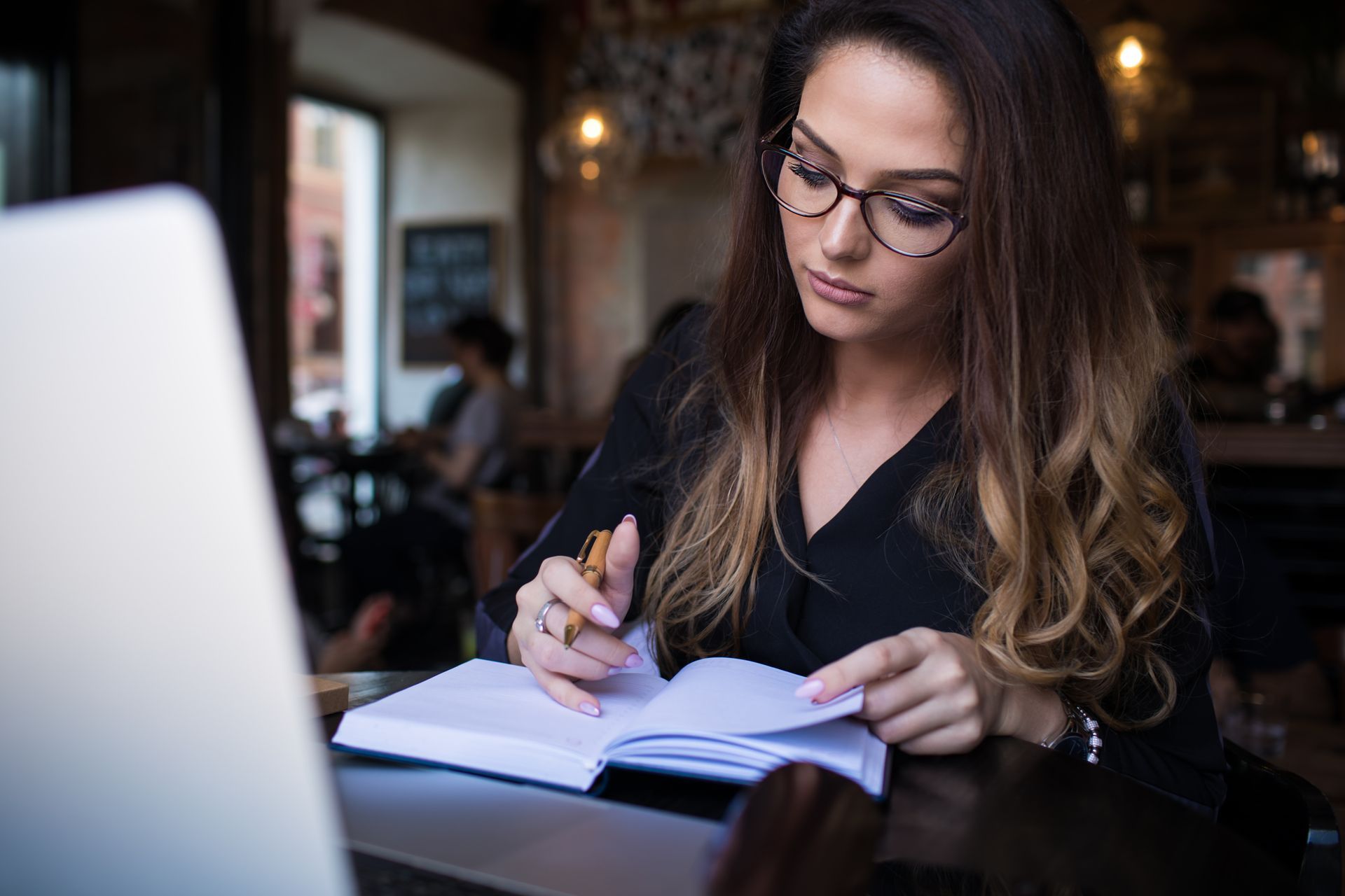 A woman is sitting at a table with a laptop and a notebook studying notary law.