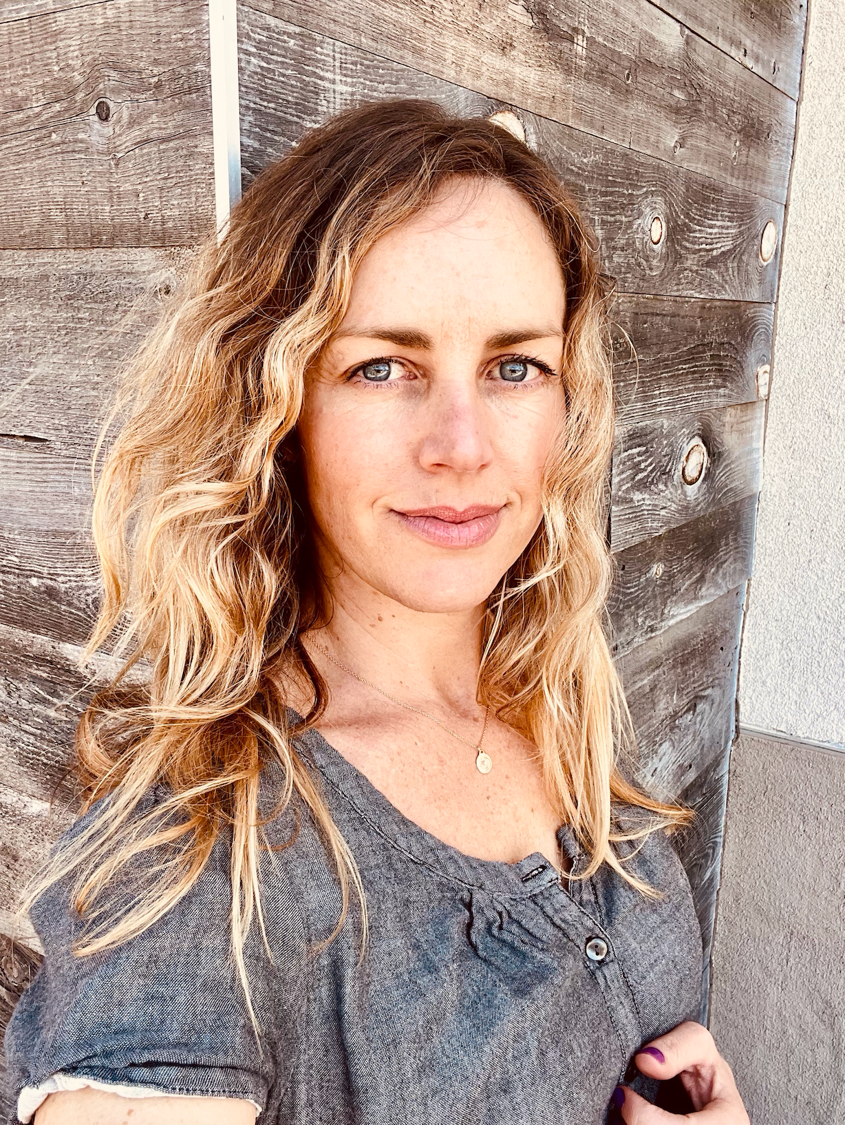 A woman with long blonde hair is standing in front of a wooden wall.