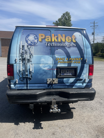 Blue PakNet Technologies van with cloud and antenna graphics, parked outdoors.