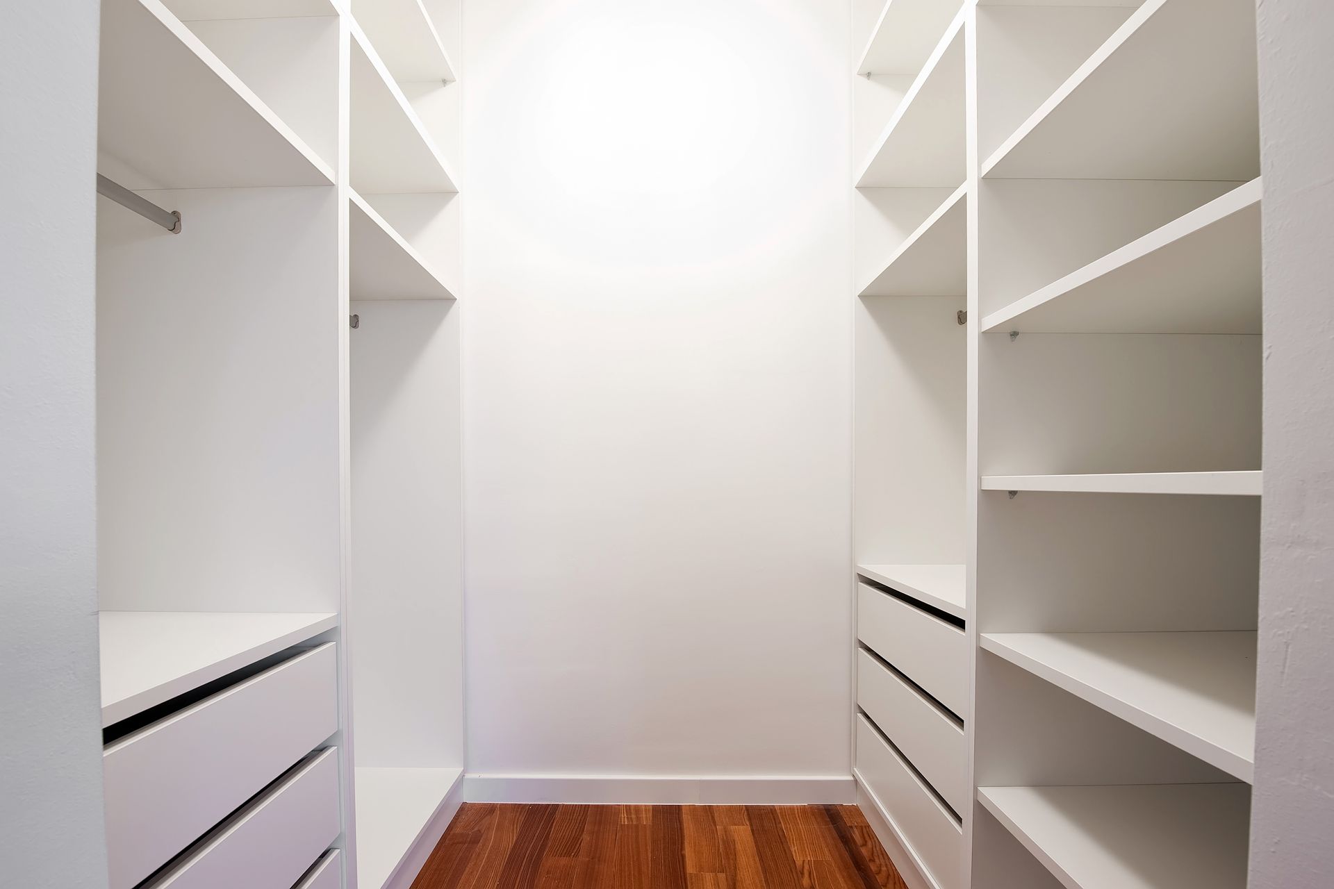 Empty Walk-in Closet With White Shelving, Drawers, and Wood Floor — Payton Kitchens in Westbrook, QLD