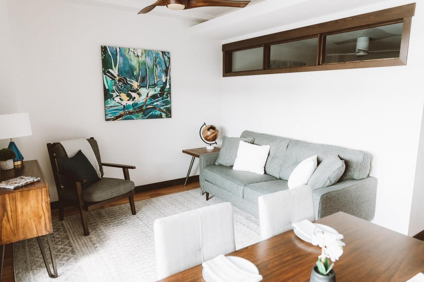 A living room with a couch , chair , table and a painting on the wall.