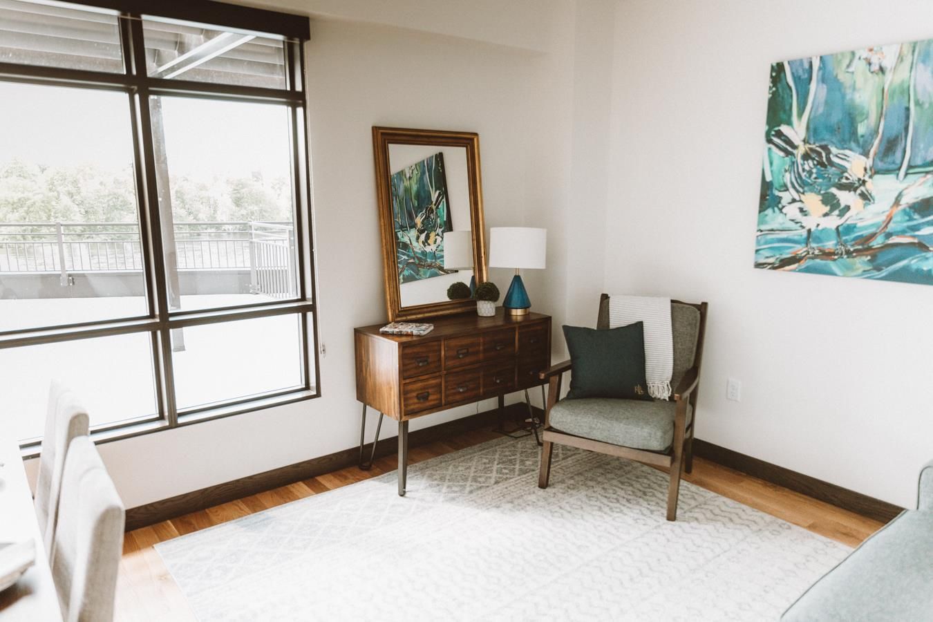 A living room with a chair , dresser , mirror and painting on the wall.