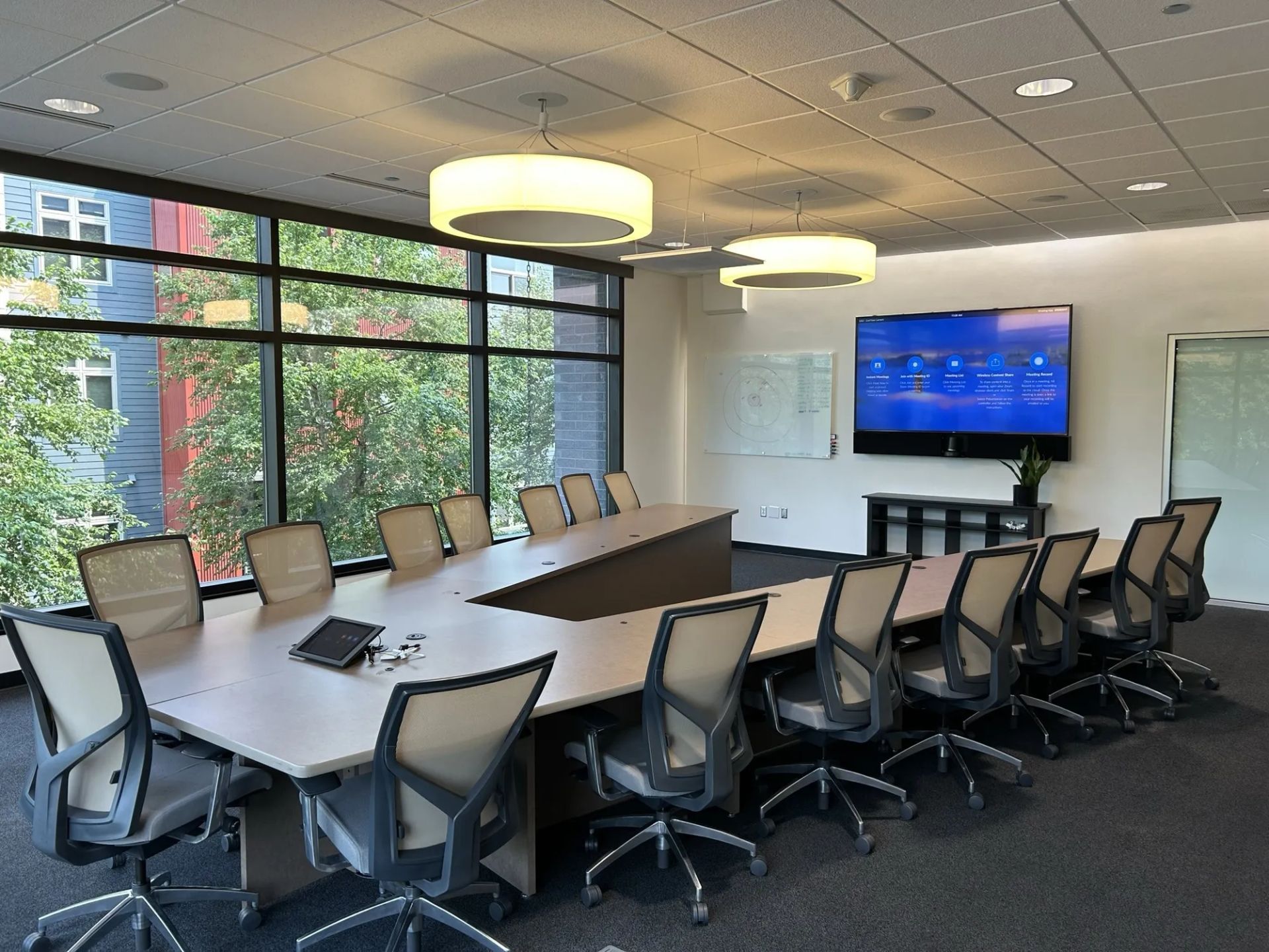 Meeting room with long table, chairs, TV, windows, and two round ceiling lights.