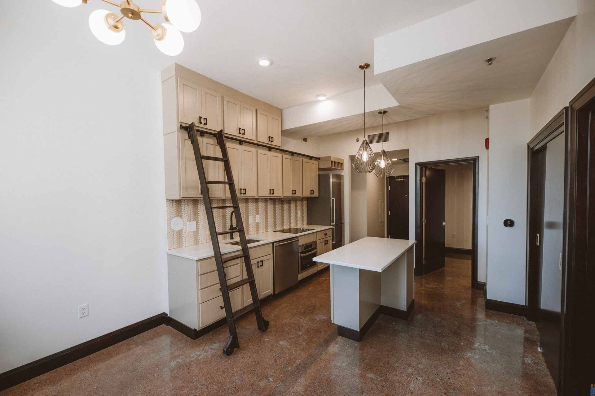 An empty kitchen with a ladder going up to the cabinets.