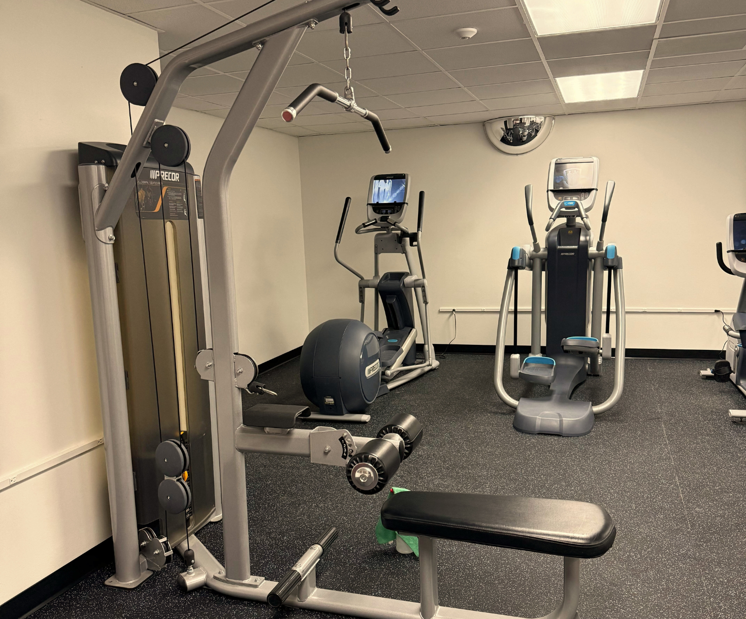 Gym with a lat pulldown machine, ellipticals, and weights on a black and gray floor.