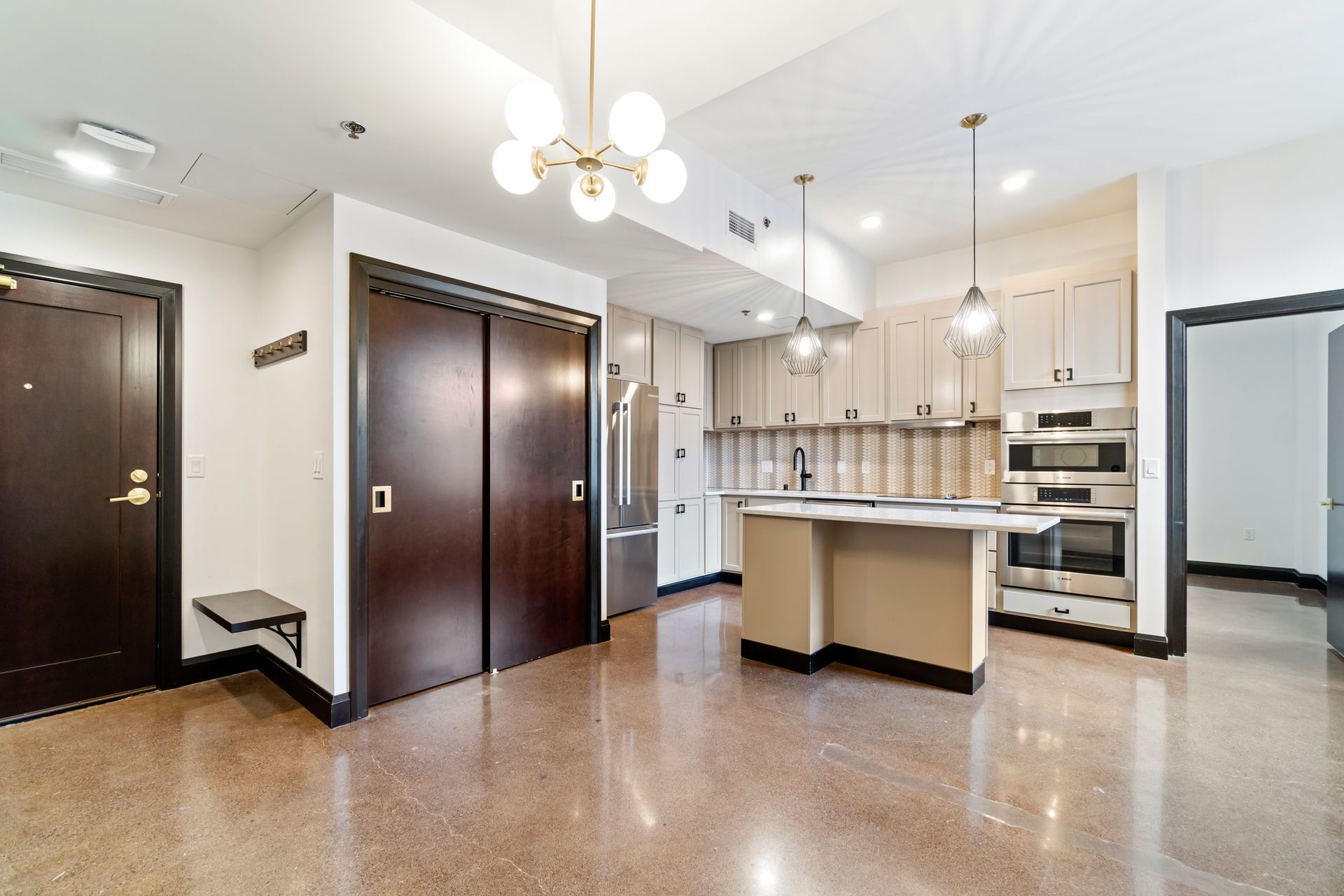 Modern kitchen with cabinets, island, and stainless steel appliances, lit by pendant lights.