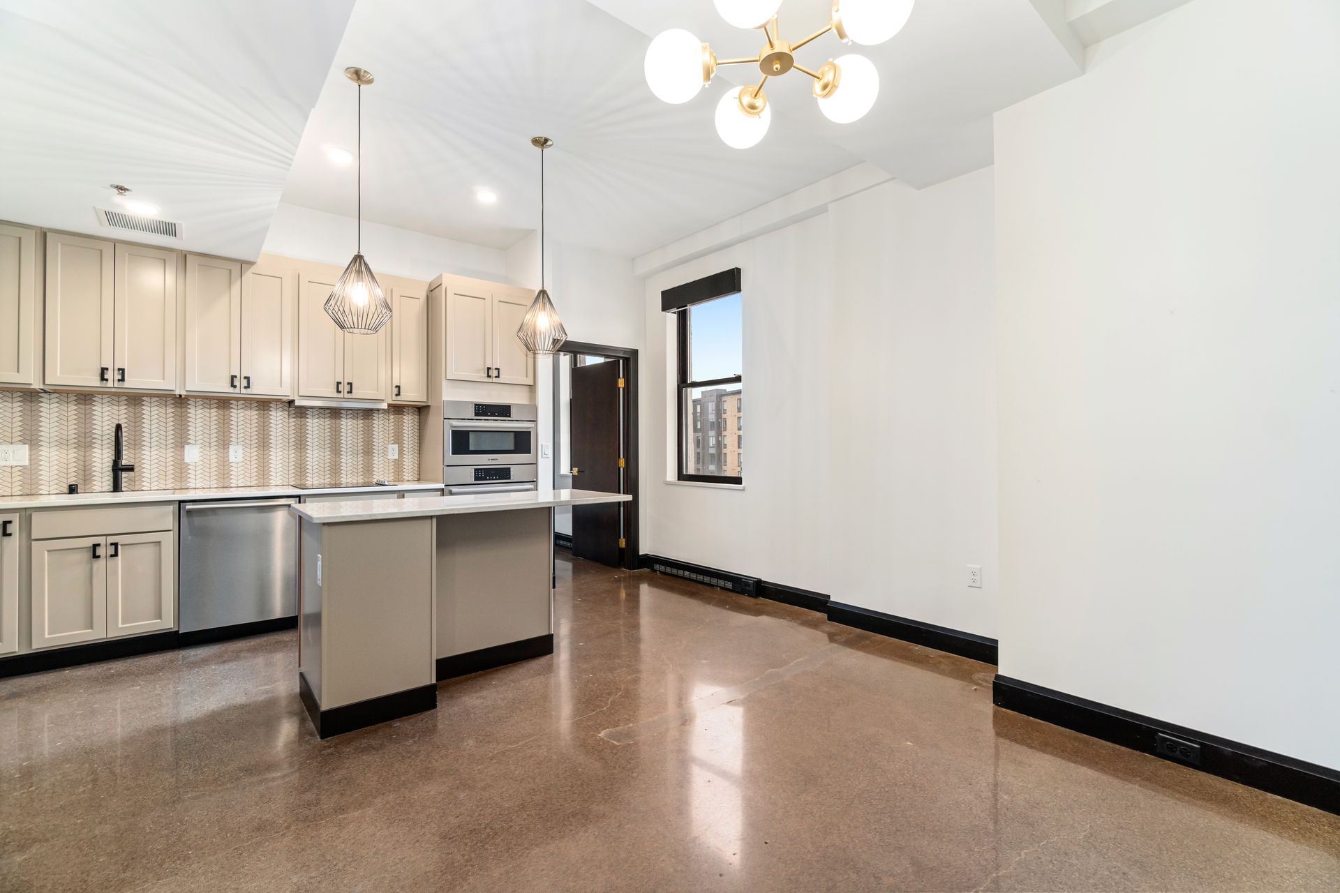 Modern kitchen with island, beige cabinets, stainless appliances, and polished concrete floors.