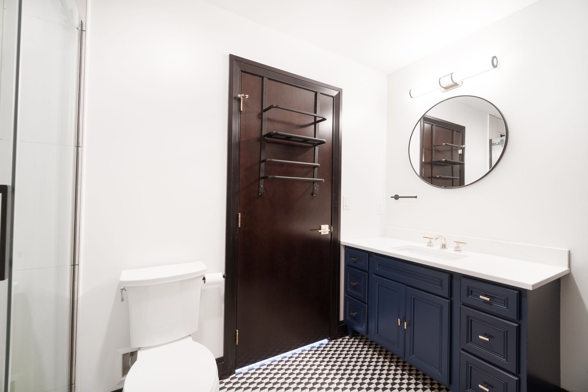 Bathroom with navy vanity, black and white tiled floor, and dark brown door with shelves.