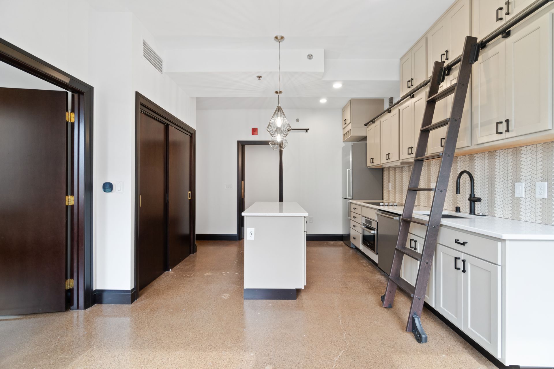 Modern kitchen with white cabinets, island, ladder, and doorway.