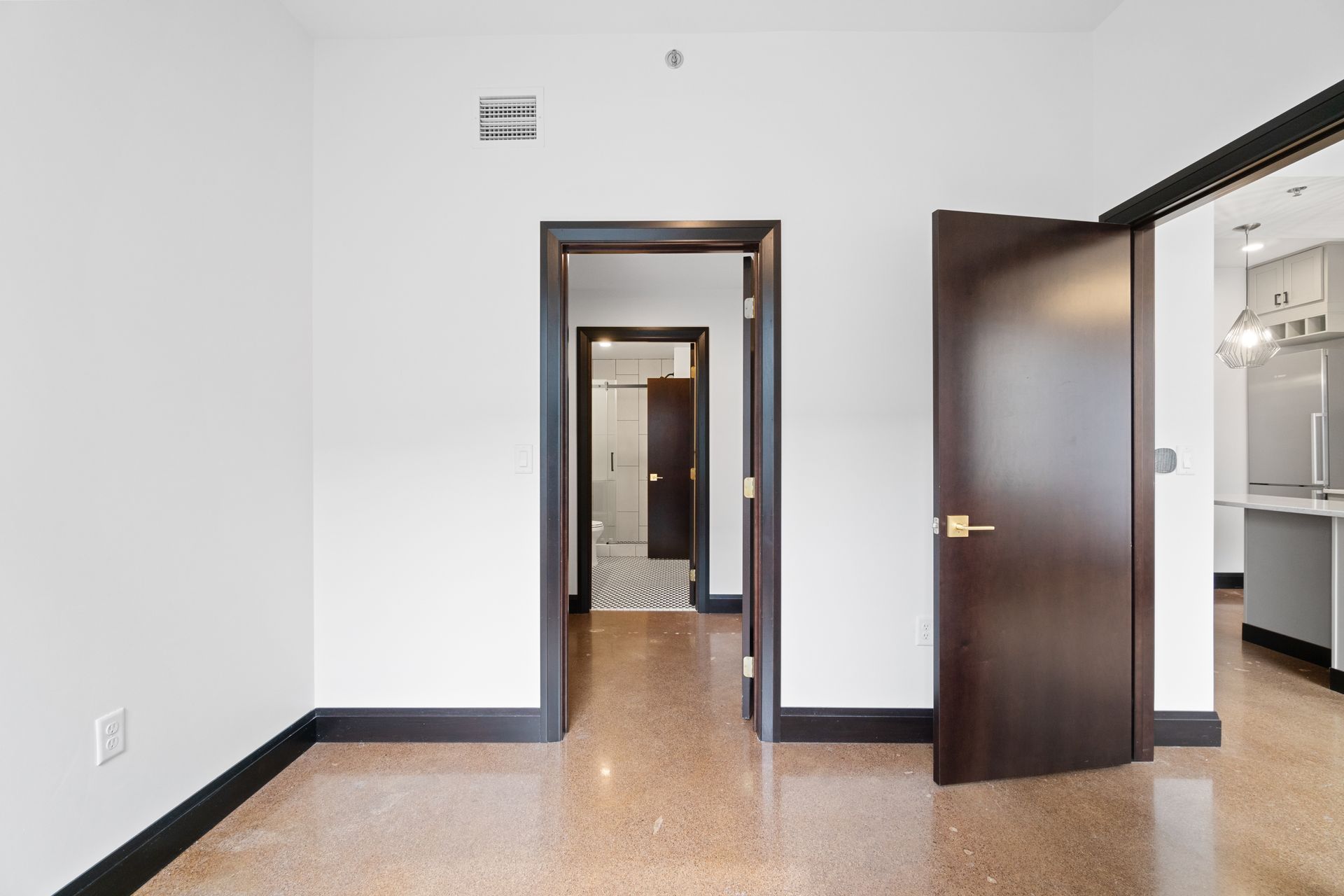 Empty room with three dark-framed doorways, white walls, and speckled flooring.