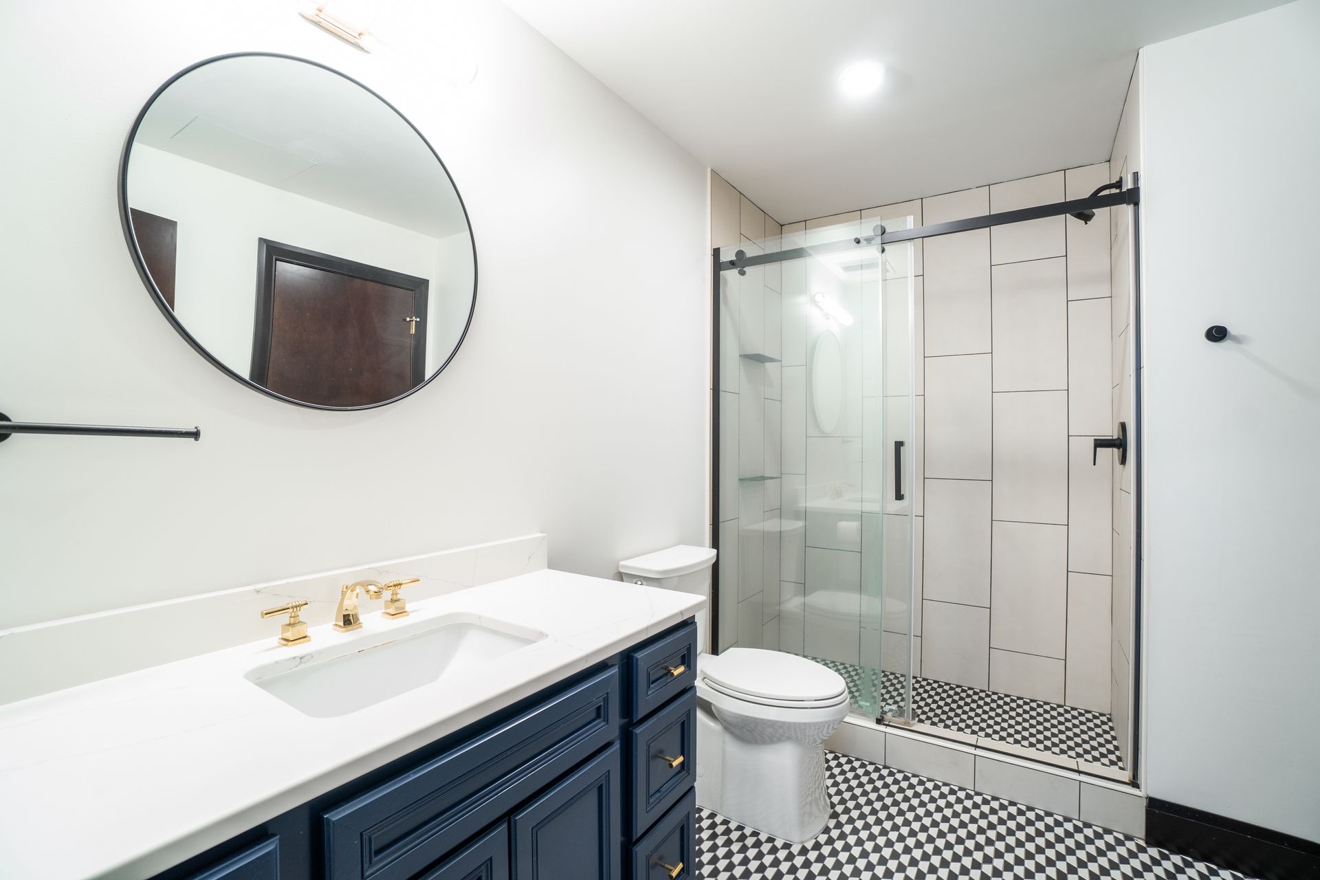 Modern bathroom with navy blue vanity, gold fixtures, black and white tile, and glass shower.