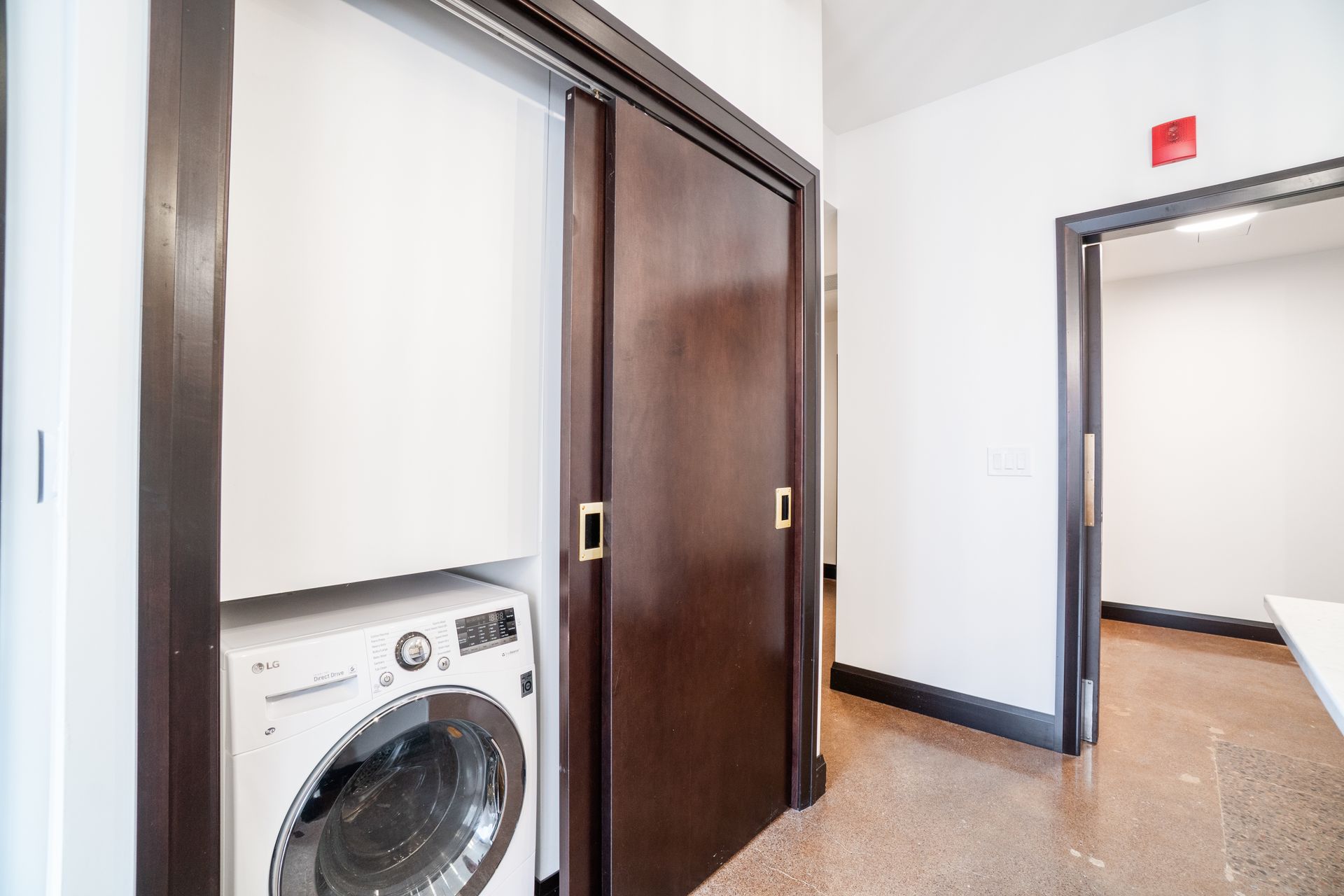 Washer/dryer under sliding door in hallway; brown trim; door to room on right.