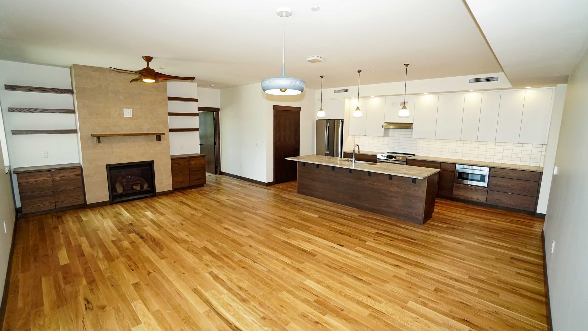 A living room with hardwood floors , a fireplace , and a kitchen.