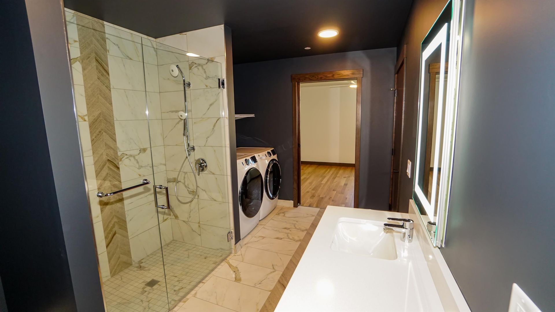 A bathroom with a sink , washer and dryer and a walk in shower.