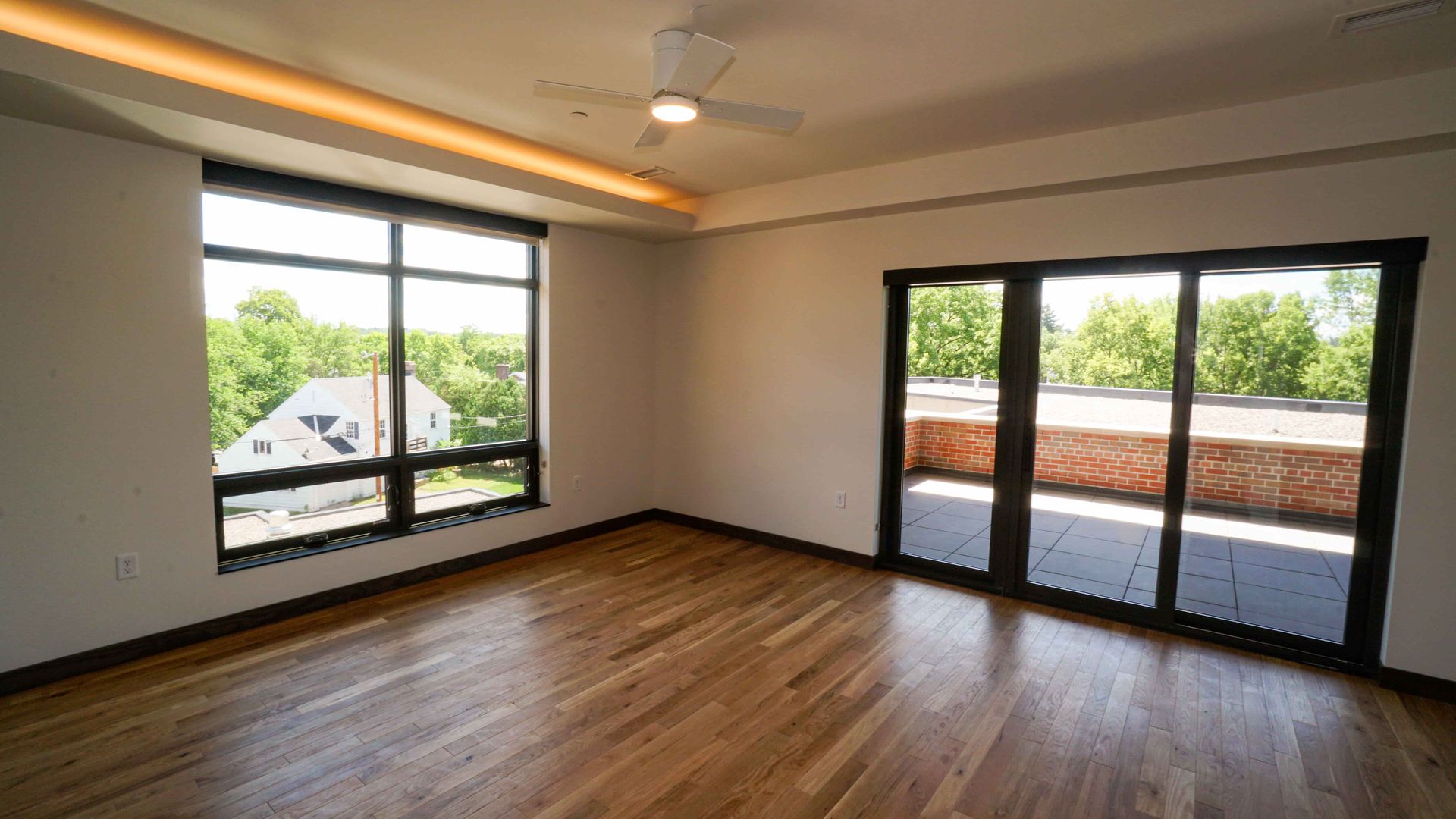 An empty living room with hardwood floors , sliding glass doors , and a ceiling fan.