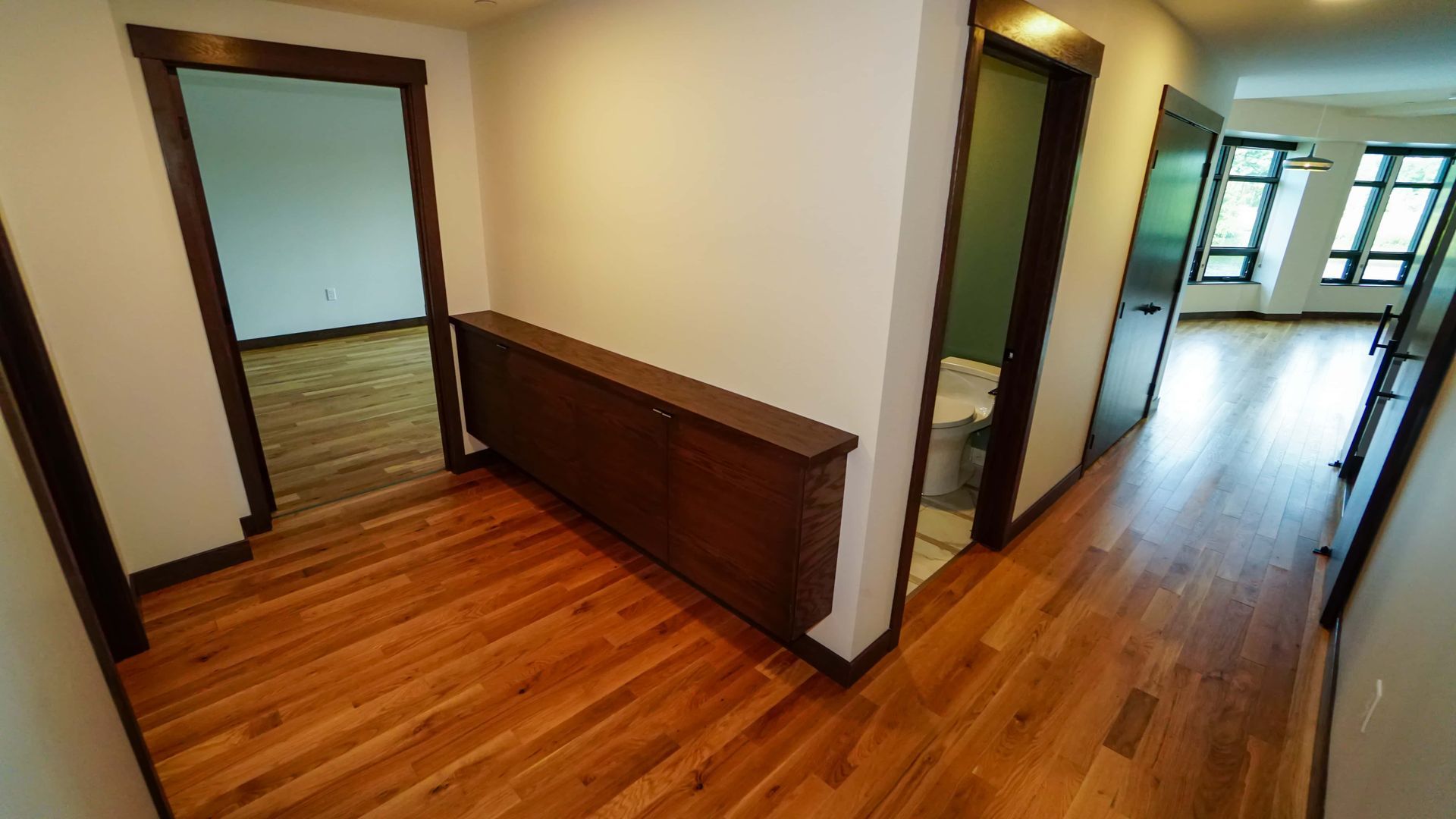 An empty hallway with hardwood floors and a toilet