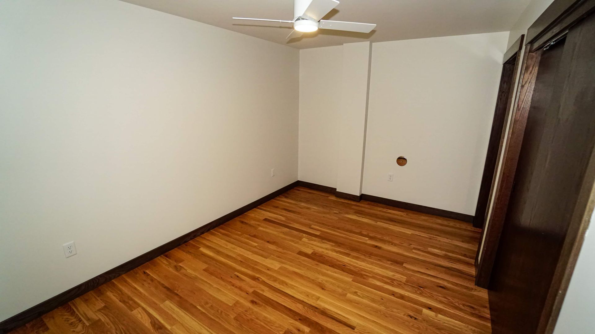 An empty room with hardwood floors and a ceiling fan.