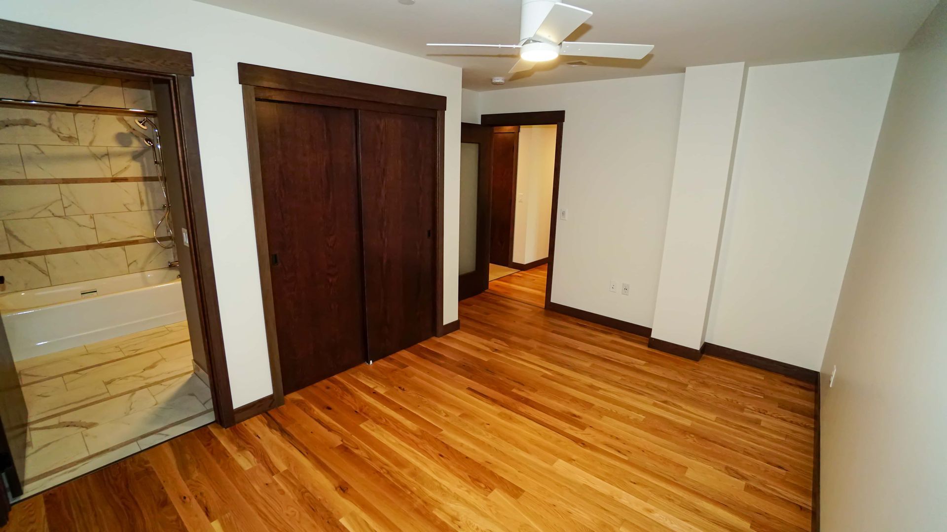 An empty bedroom with hardwood floors and a ceiling fan.