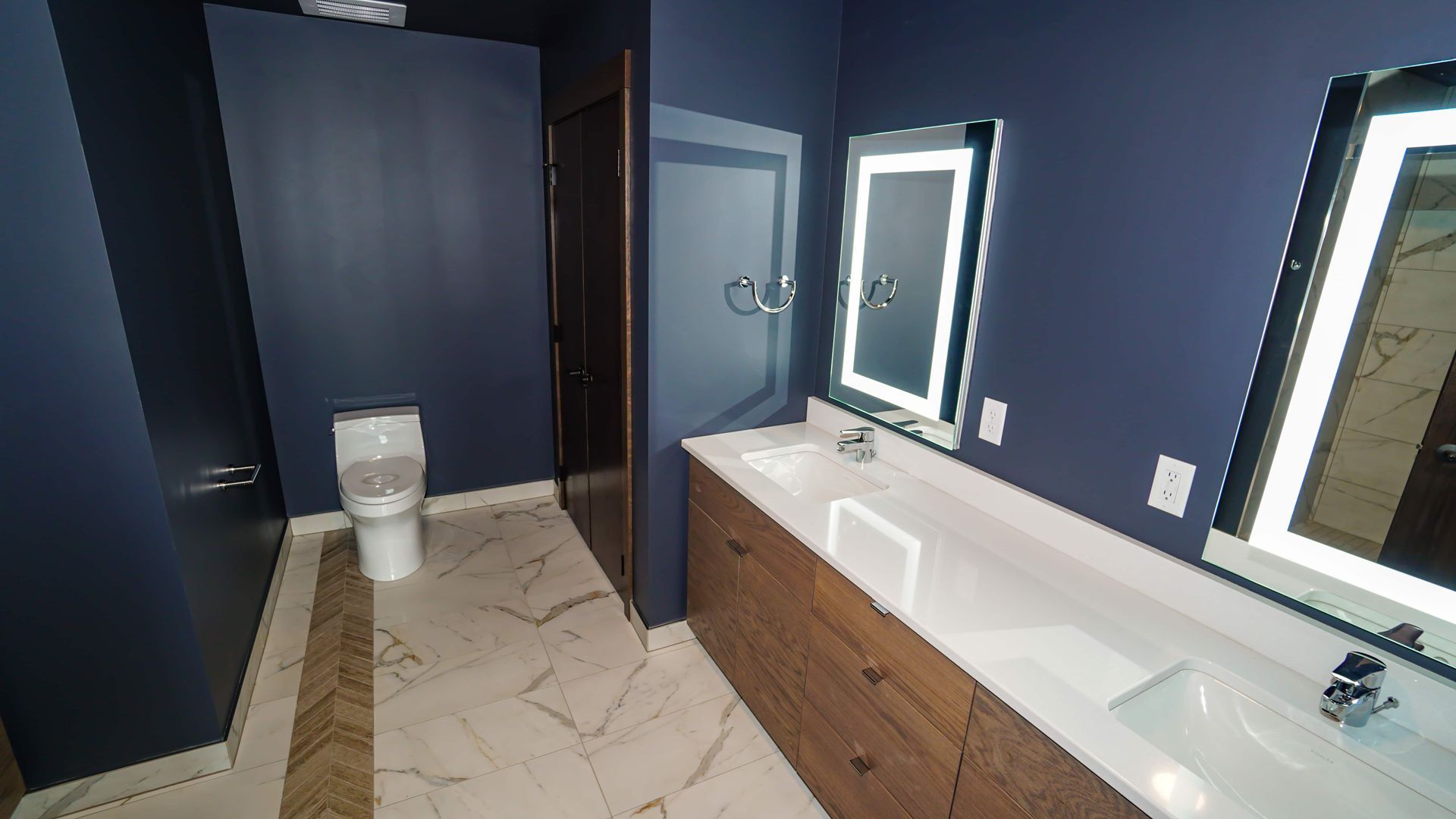 A bathroom with two sinks , a toilet and two mirrors.