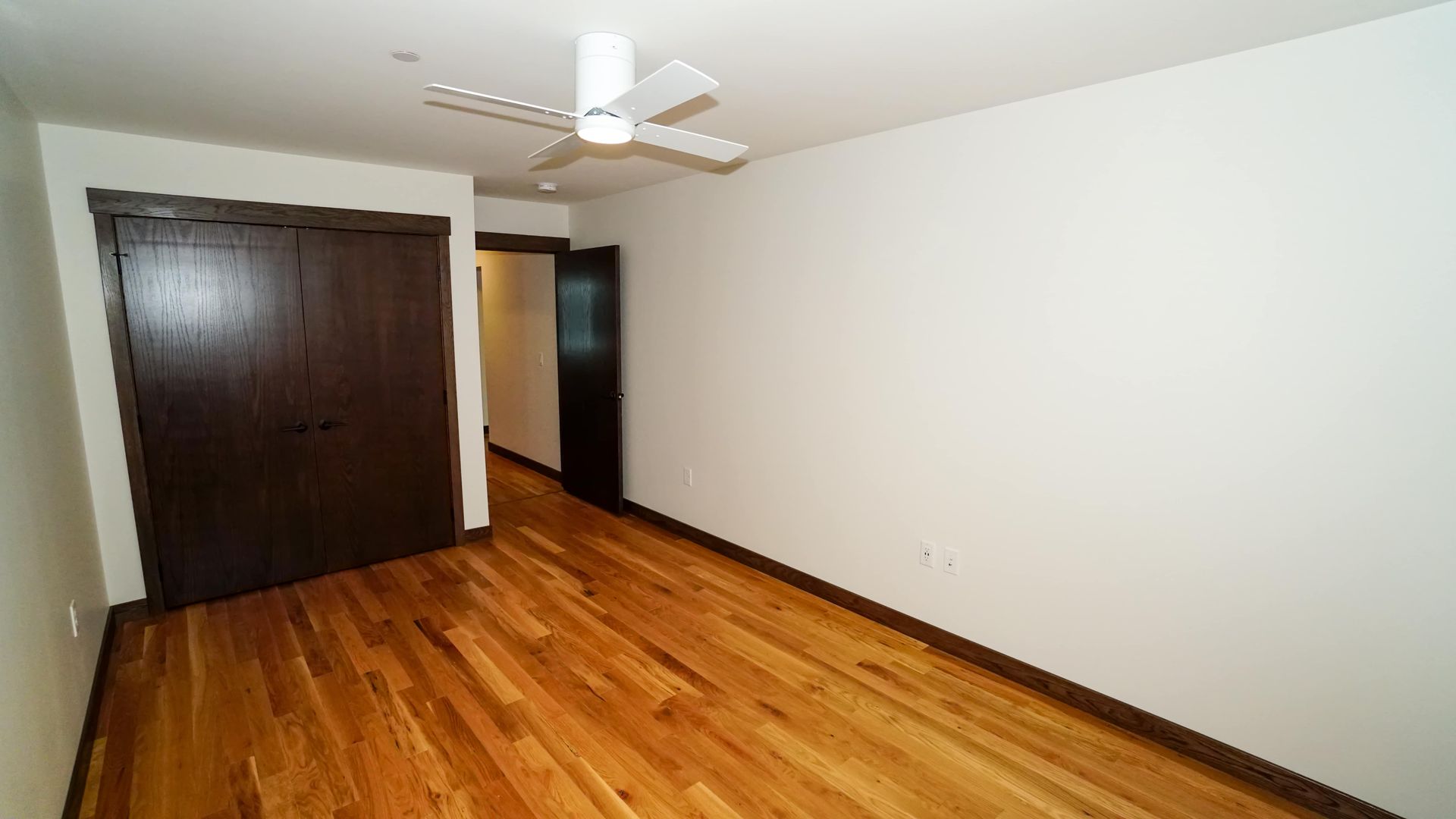 An empty bedroom with hardwood floors and a ceiling fan.