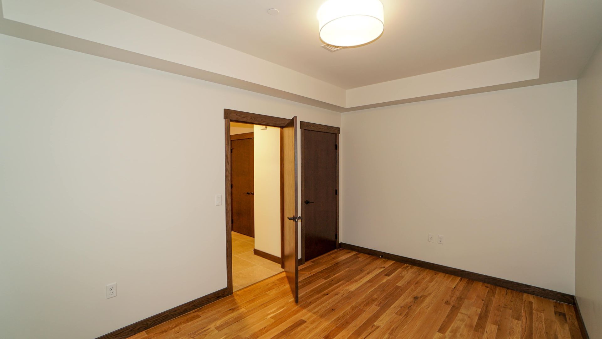 An empty bedroom with hardwood floors and white walls.