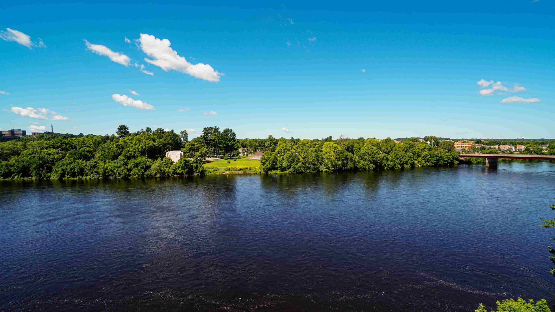 A large body of water surrounded by trees and a bridge.