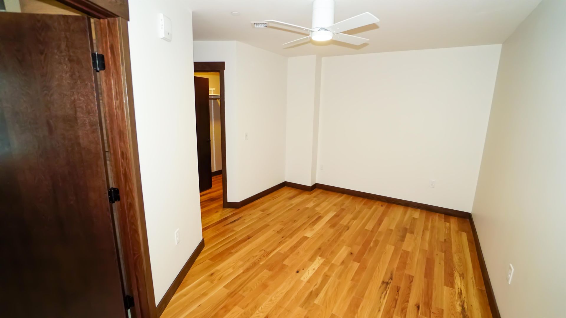 An empty room with hardwood floors and a ceiling fan.