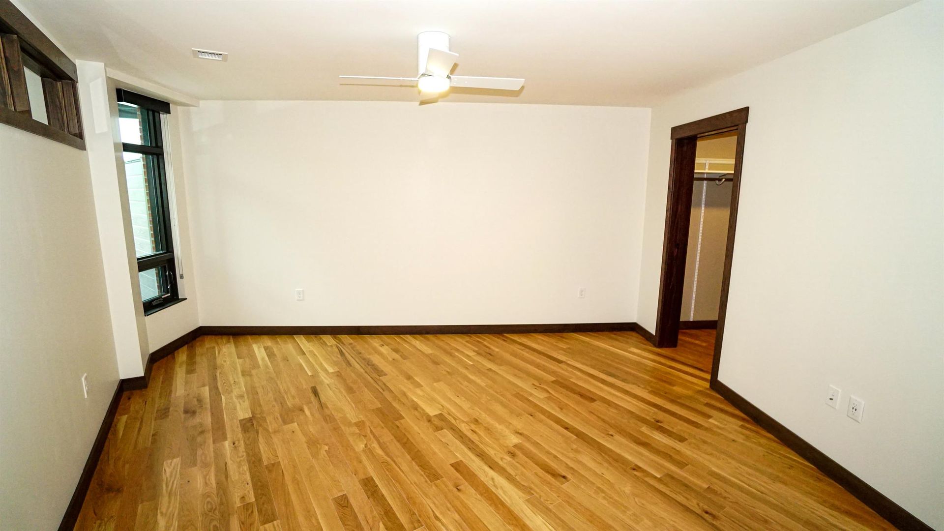 An empty living room with hardwood floors and a ceiling fan.
