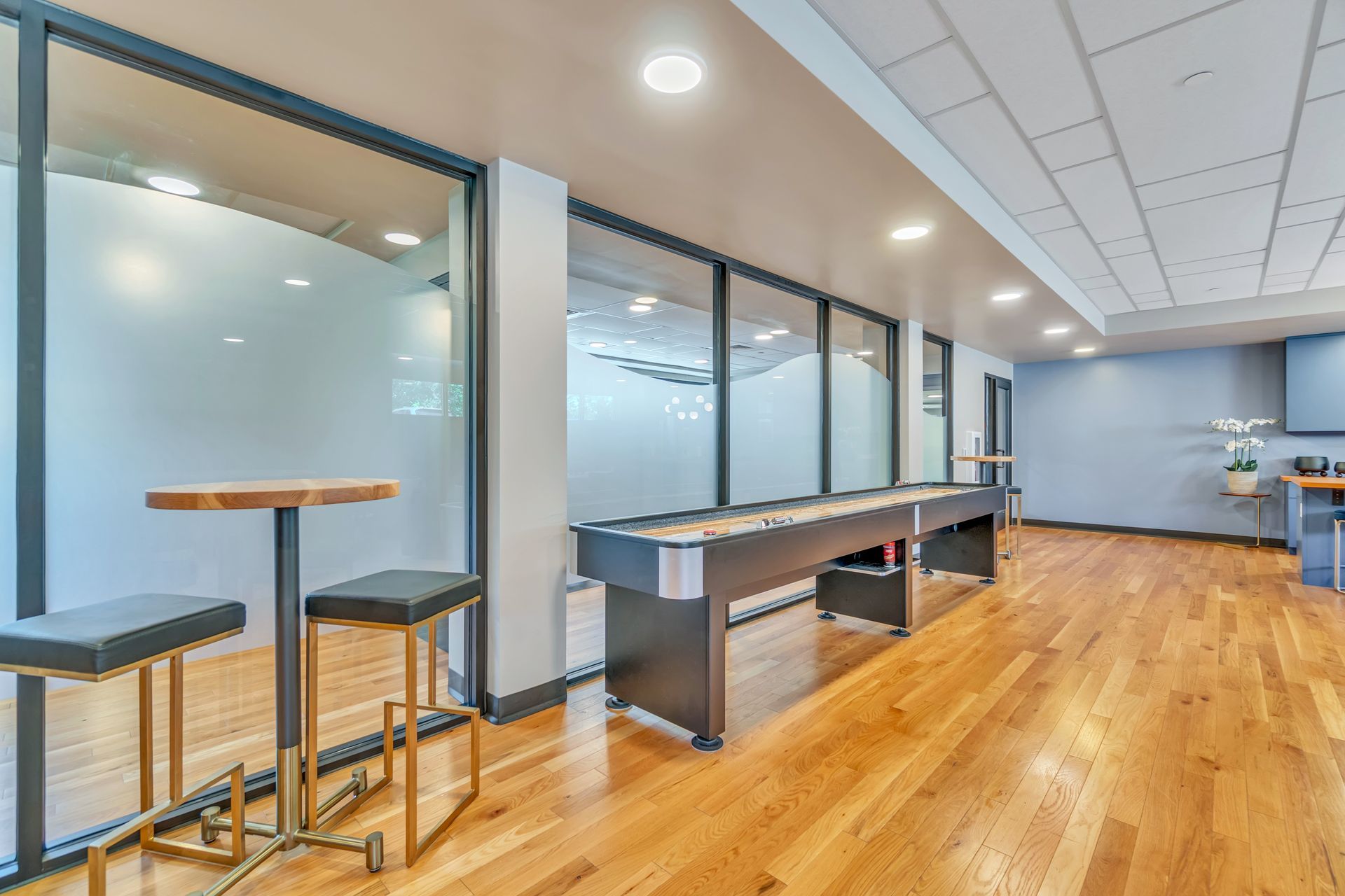 Game room with a shuffleboard table, bar stools, and large windows.