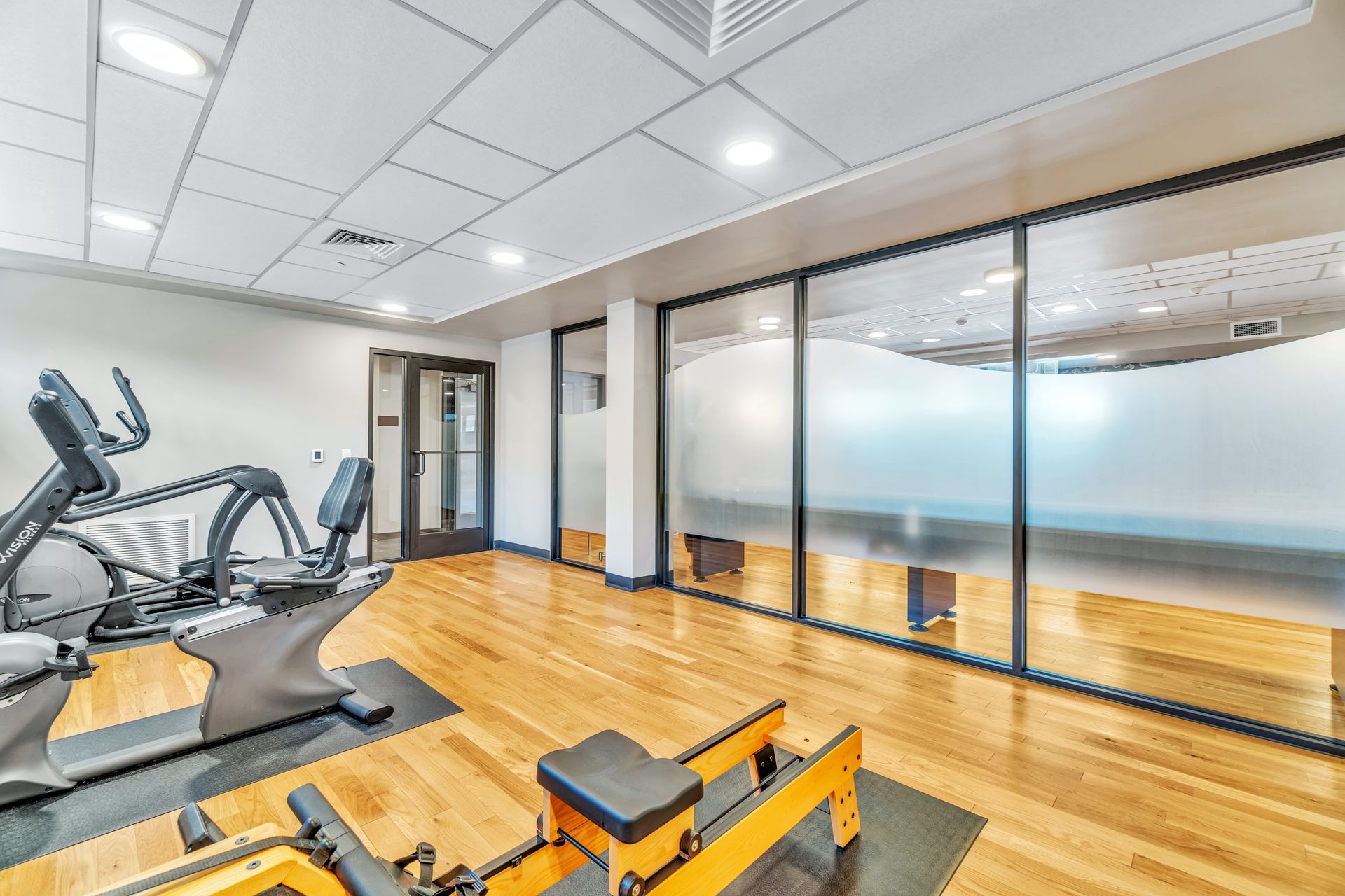 Gym with exercise equipment, wooden floor, frosted glass windows, and a door.