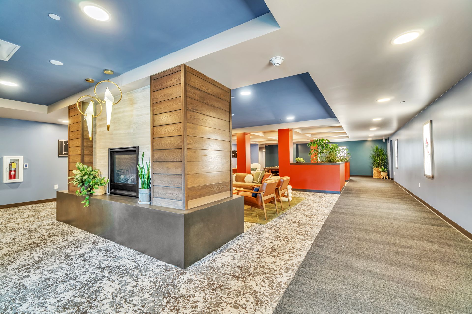 Lobby with fireplace, seating area, and long hallway. Blue ceiling, gray carpet, and wood accents.
