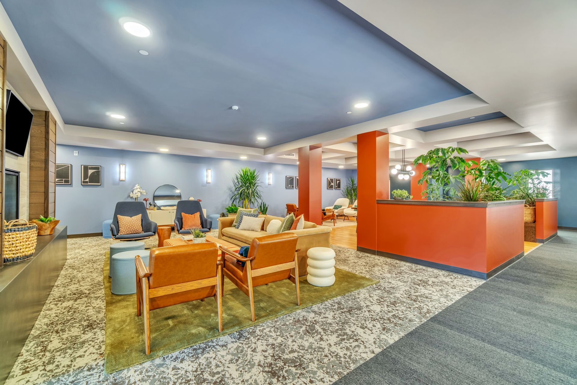 Lounge area with blue ceiling, orange accents, sofas, armchairs, plants, and patterned rugs.