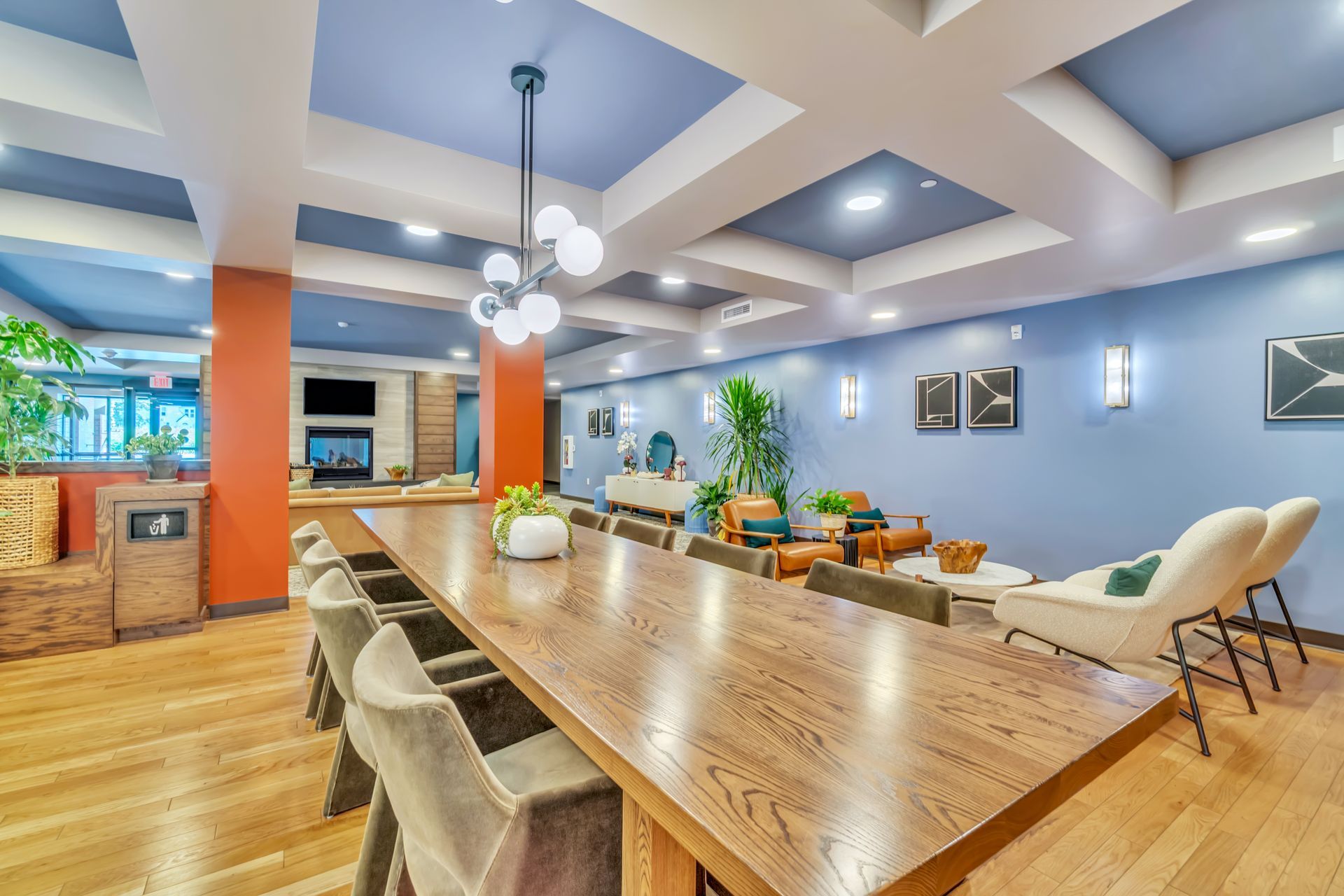 Spacious lounge with long wooden table, chairs, seating areas, and modern lighting.