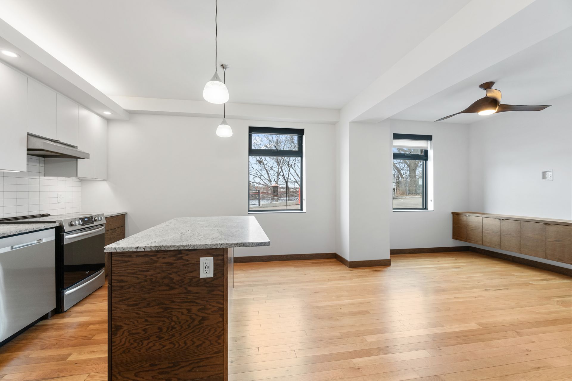 Open-concept kitchen and living space with hardwood floors, white walls, and a dark wood island.
