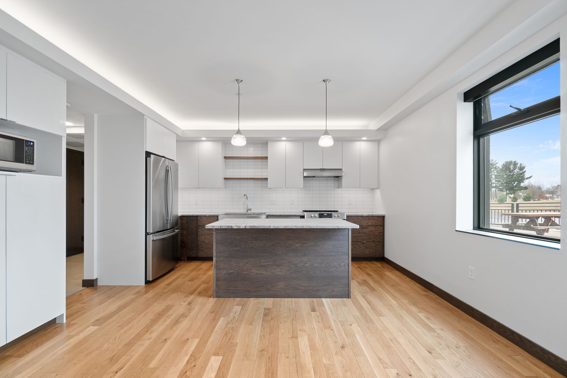 Modern kitchen with wood floors, island, stainless steel appliances, and large window.