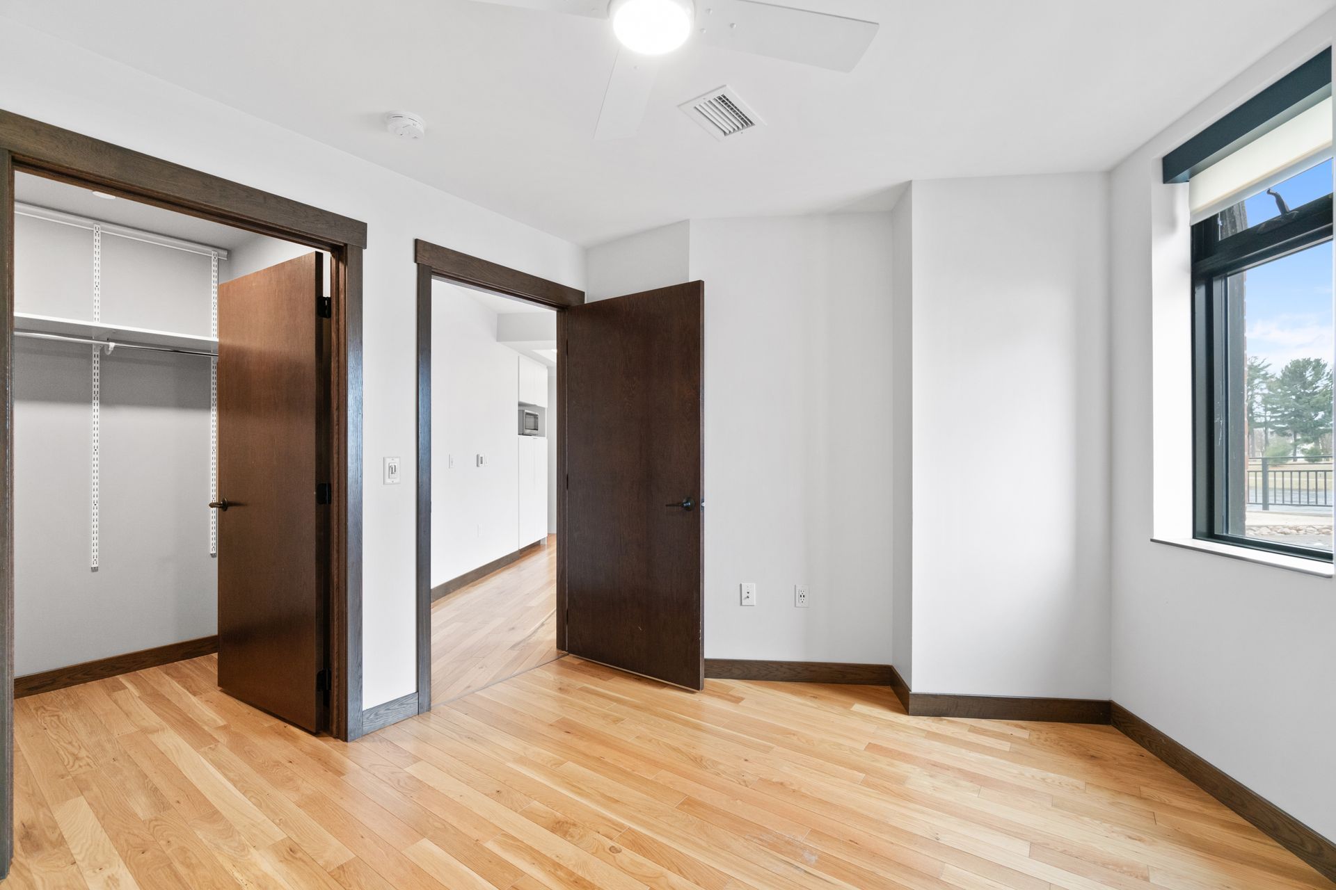 Empty bedroom with hardwood floors, closet, and window. White walls, brown trim.