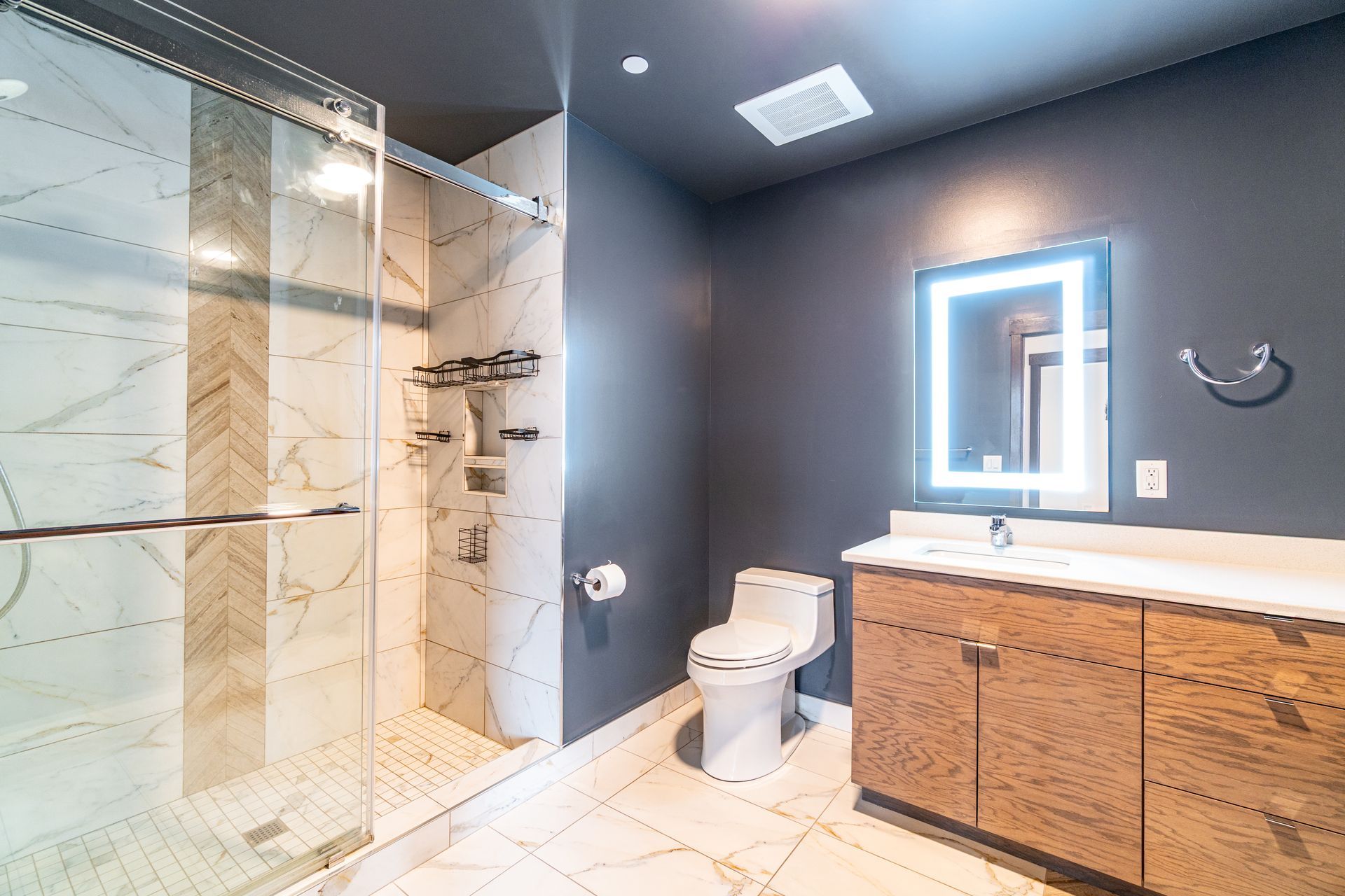 Modern bathroom with marble shower, wooden vanity, and gray walls.