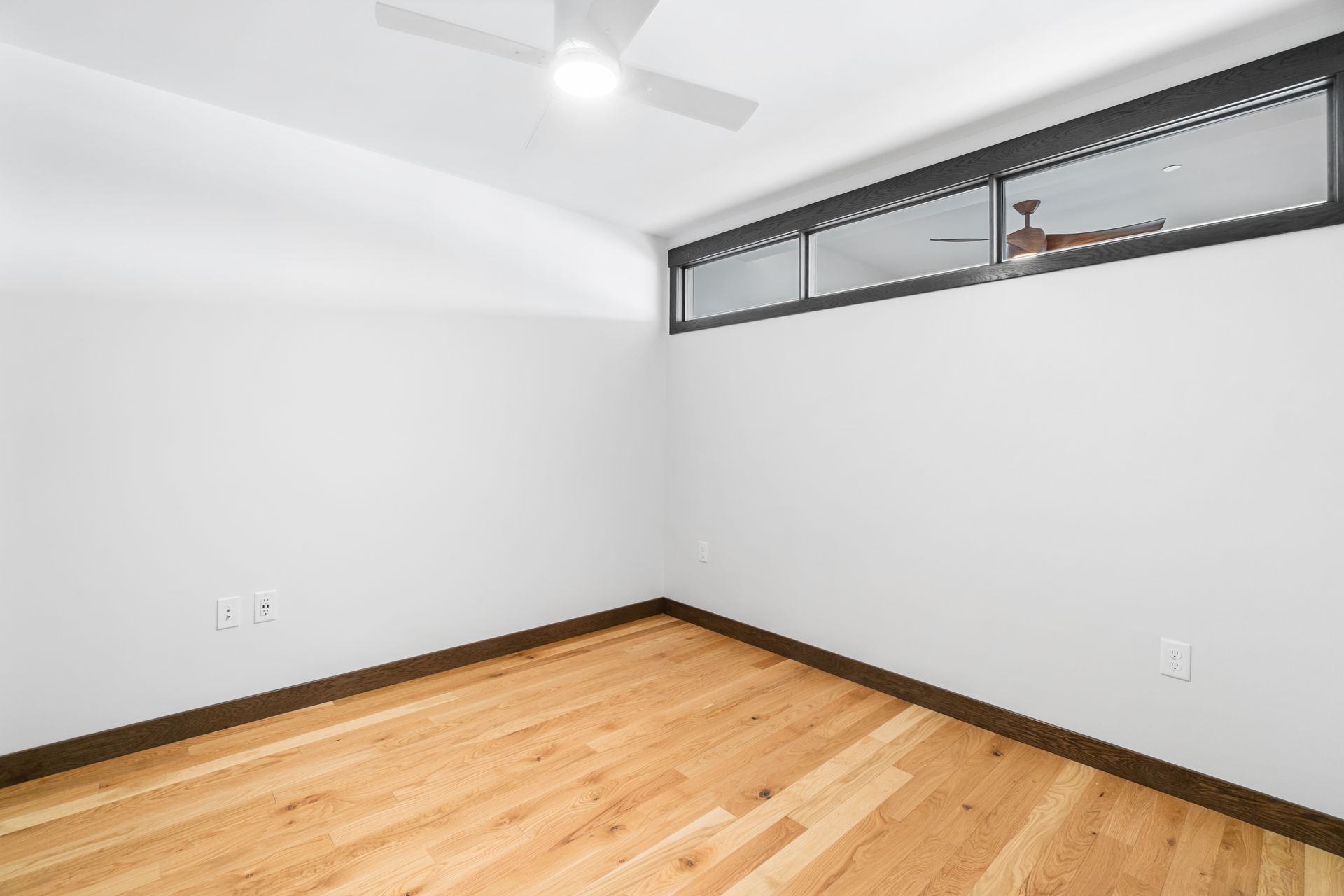 Empty room with hardwood floors, white walls, and a small rectangular window near the ceiling.