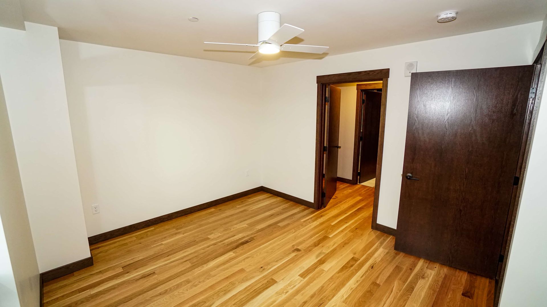 An empty room with hardwood floors and a ceiling fan.