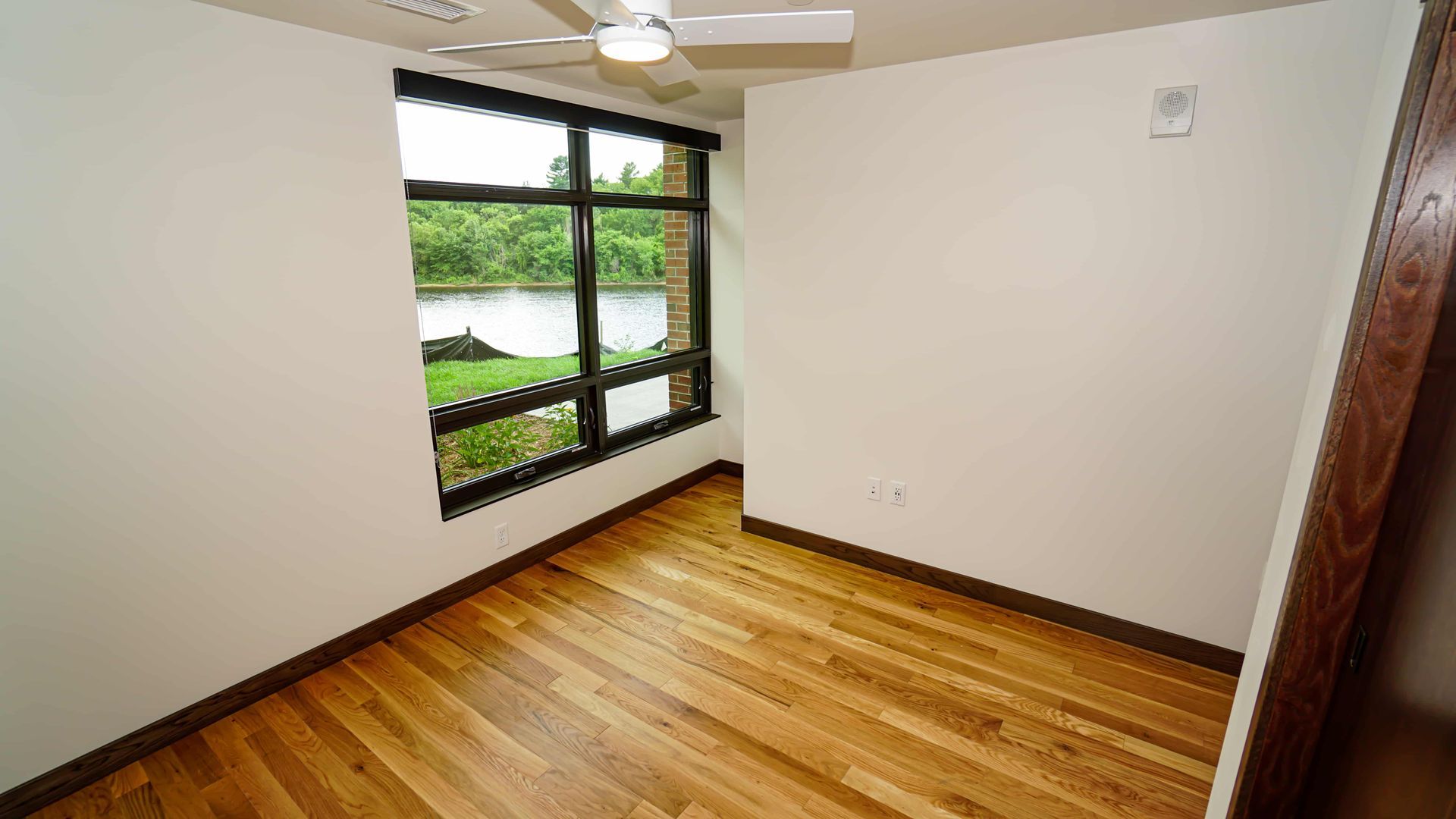 An empty room with hardwood floors and a large window with a view of a lake.
