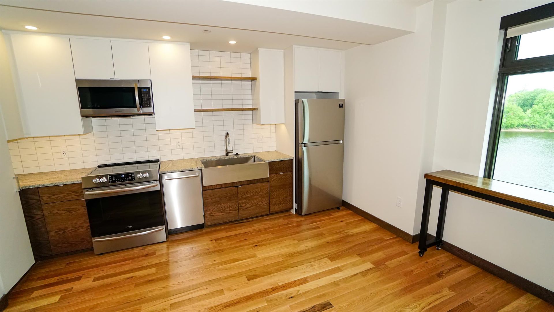 An empty kitchen with stainless steel appliances and hardwood floors