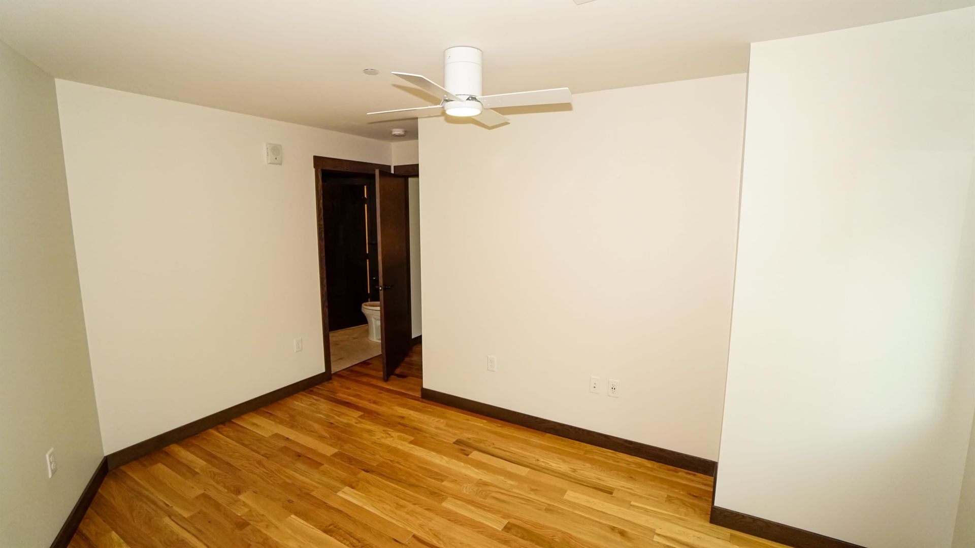 An empty room with hardwood floors and a ceiling fan.