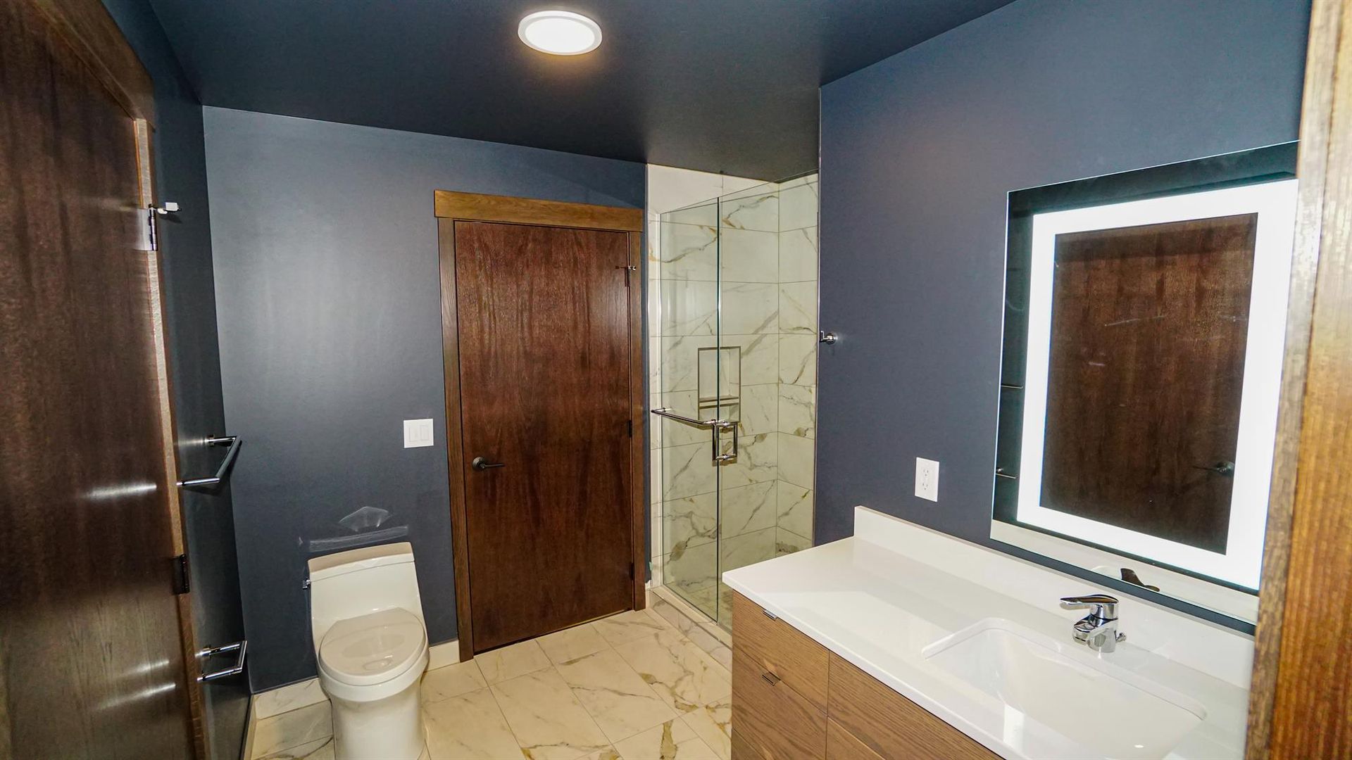 A bathroom with a toilet , sink , mirror and walk in shower.