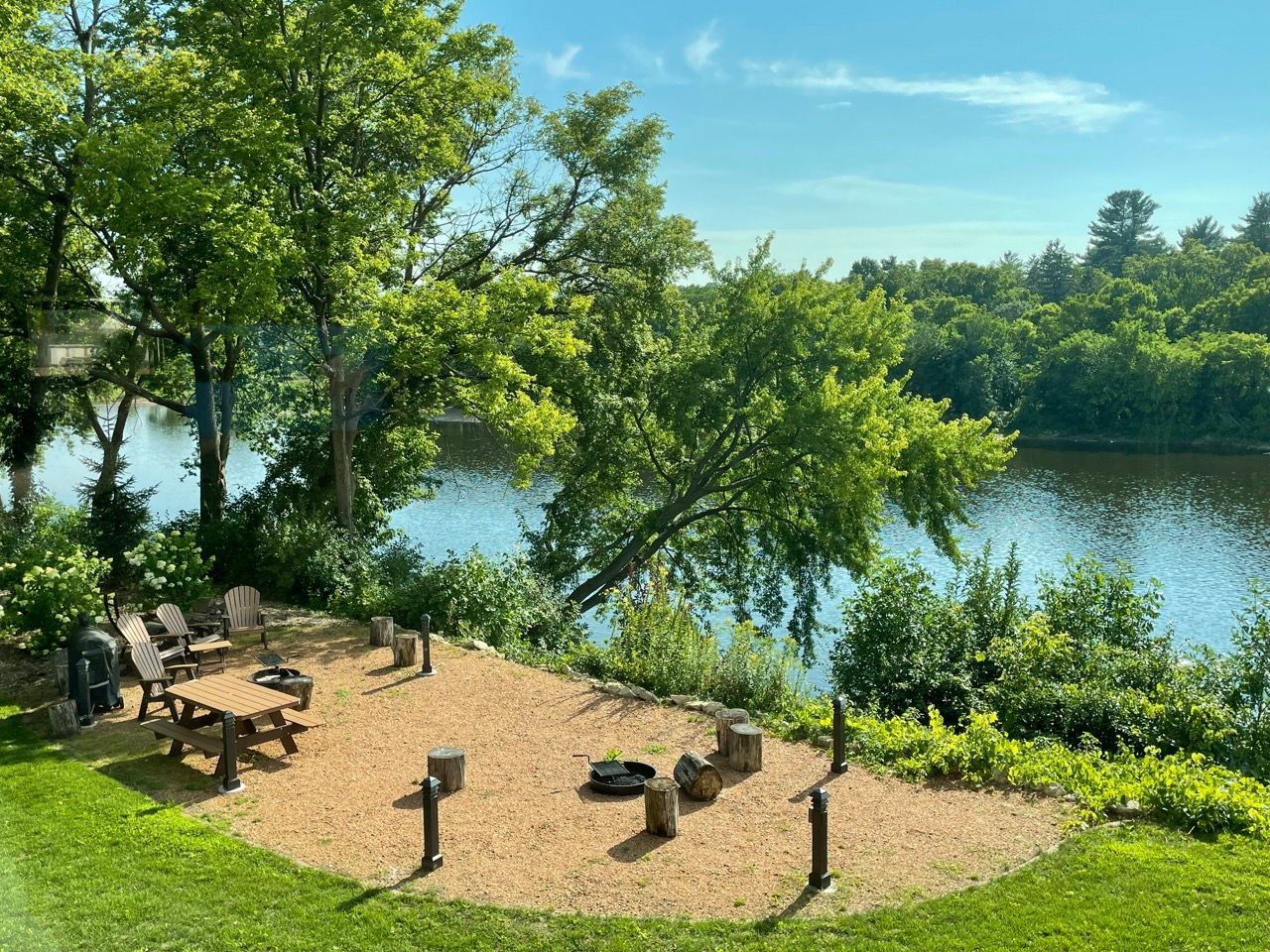 There is a fire pit in the middle of the grass next to a lake.